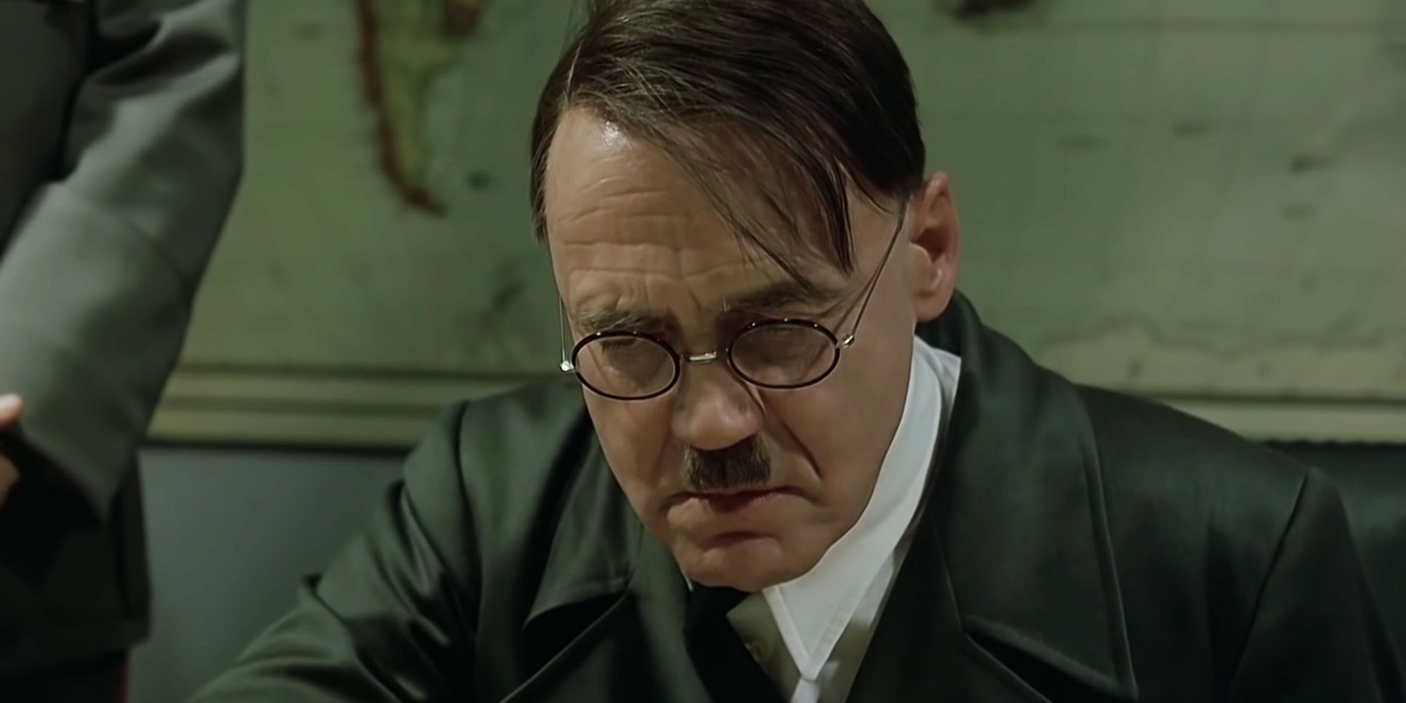 Adolf Hitler wears glasses and looks down intently at something in Downfall