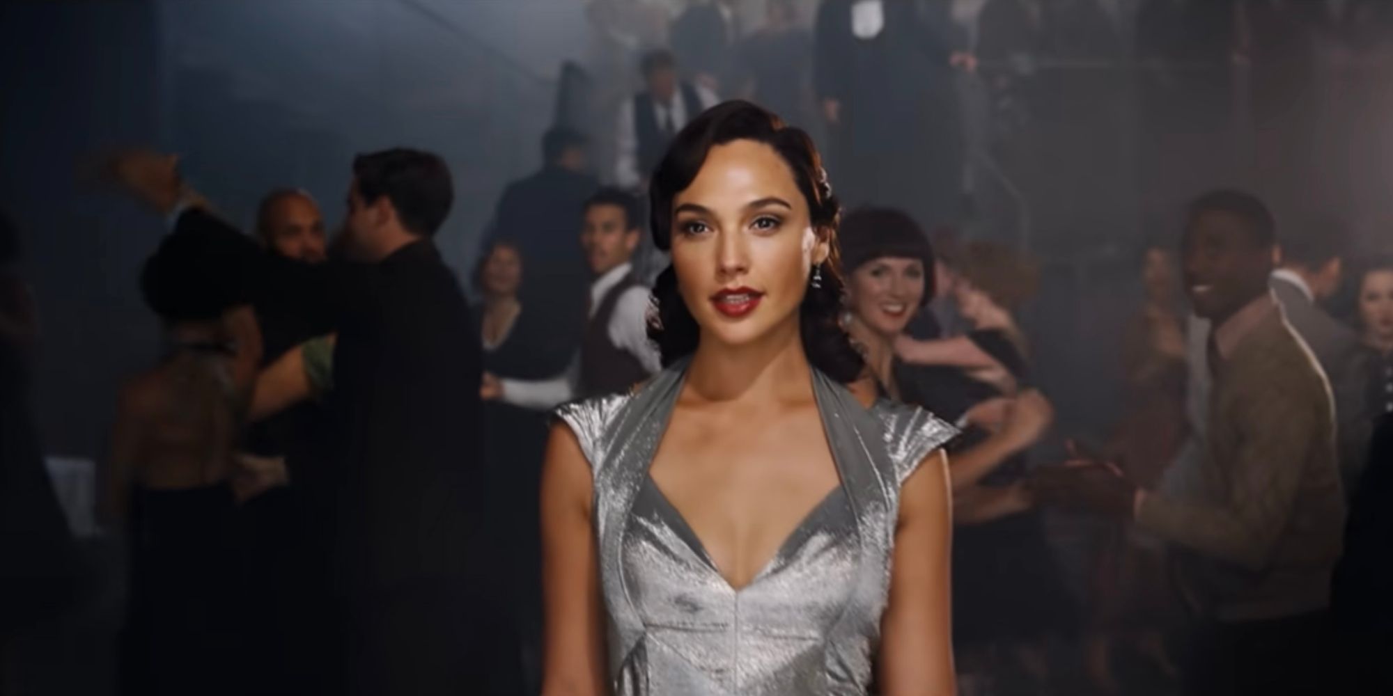 Gal Gadot as Linnet walking into a club wearing a gray dress in Death on the Nile