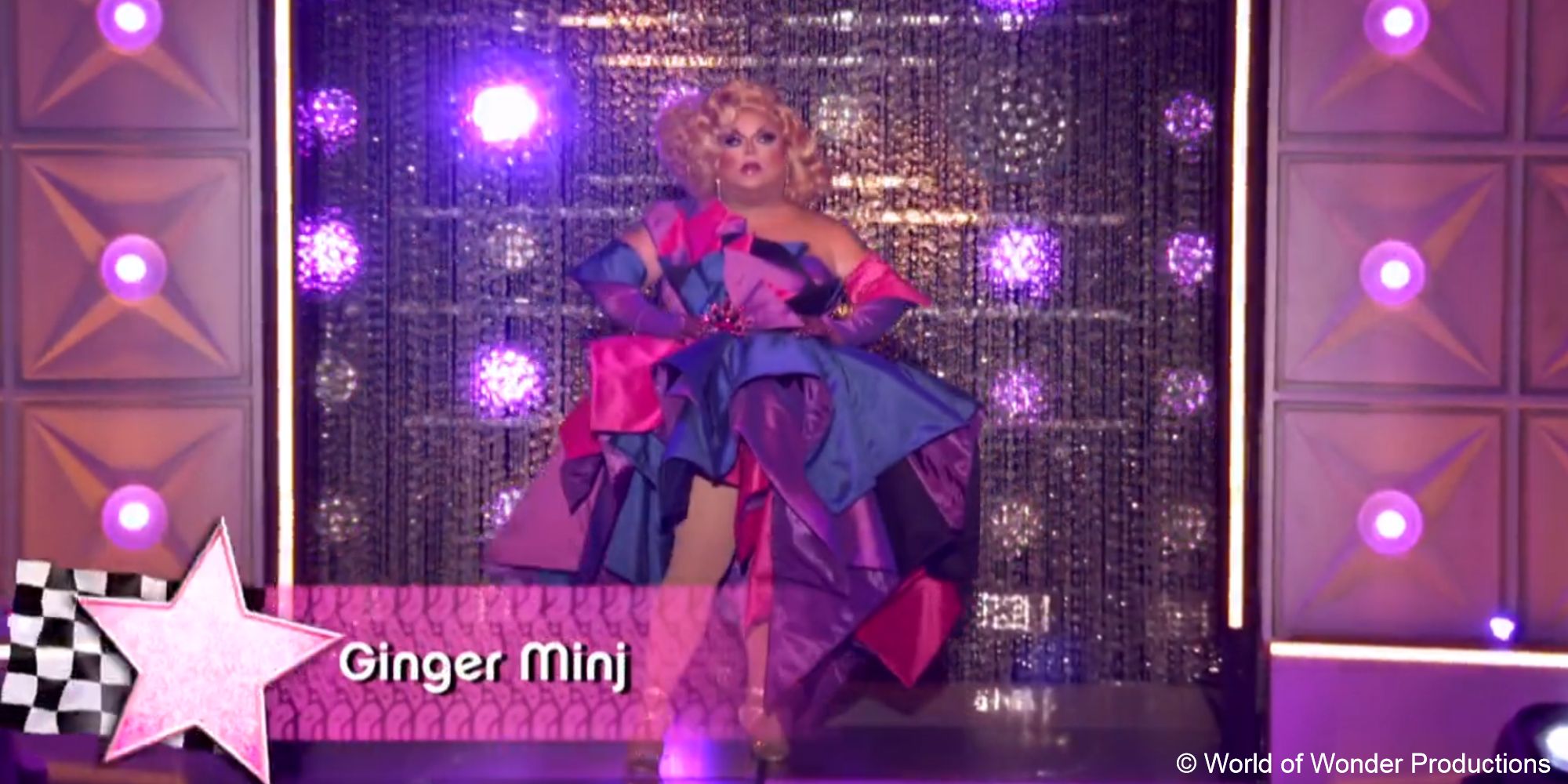 A still of drag queen Ginger Minj wearing a frilly blue, pink, and purple gown