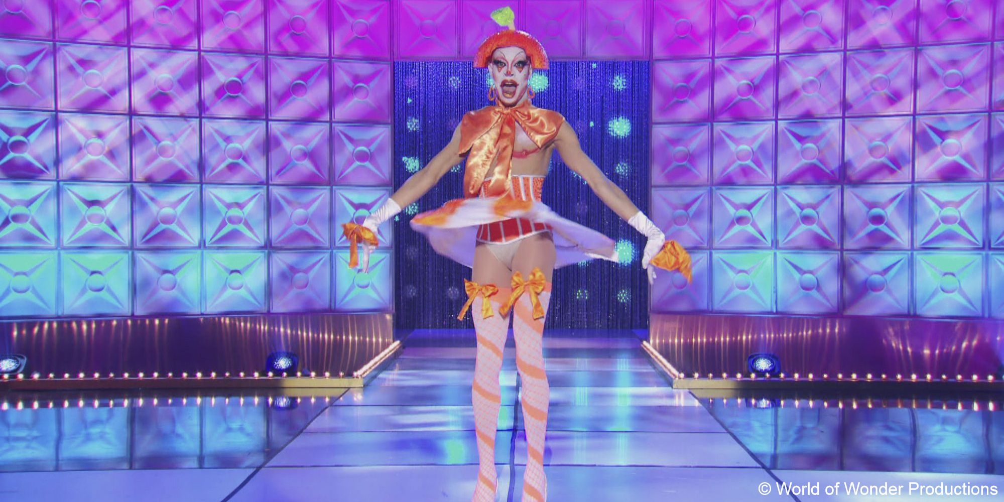 A still of drag queen Yvie Oddly wearing an orange tutu outfit, including a citrus headpiece