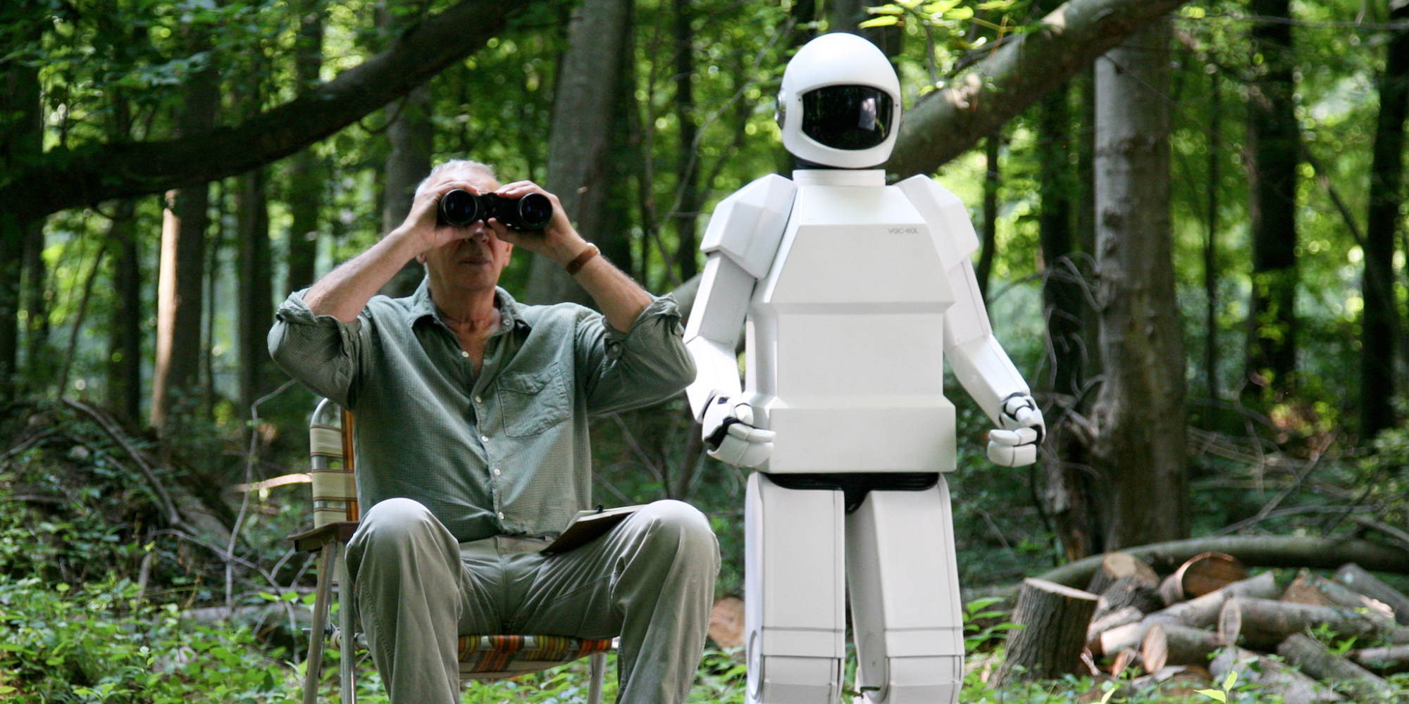 Robot e Frank na floresta enquanto Frank usa um par de binóculos 