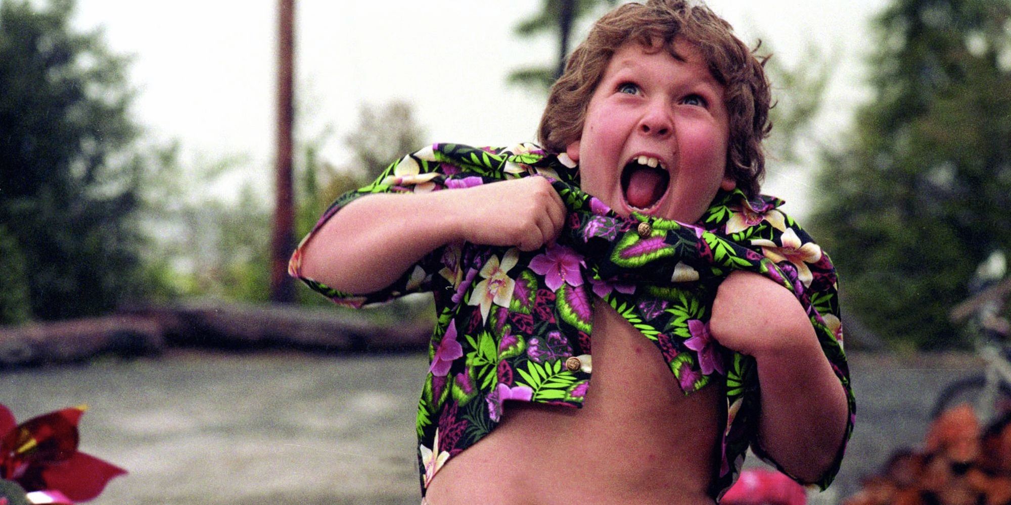 Jeff Cohen as Chunk smiling with his mouth open and his shirt pulled up in a scene from The Goonies