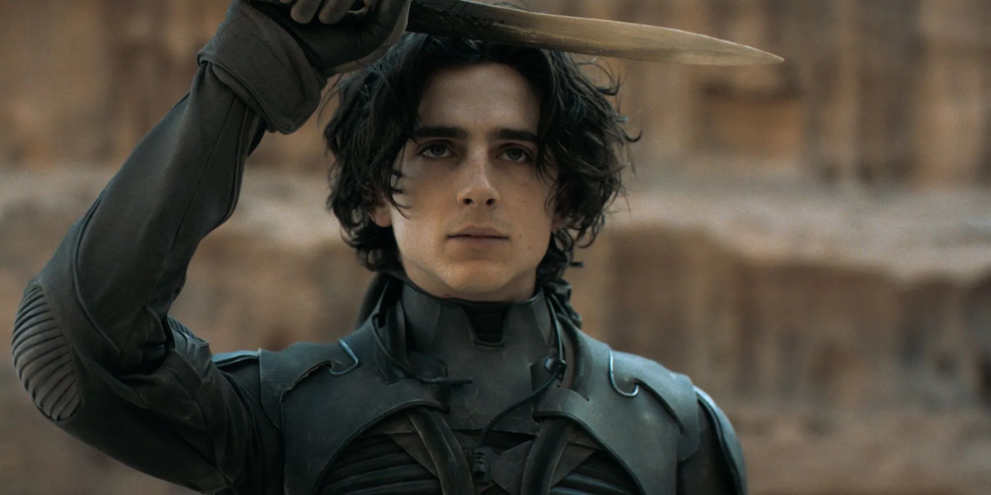 Timothee Chalamet as Paul Atreides raising a dagger over his head in Dune