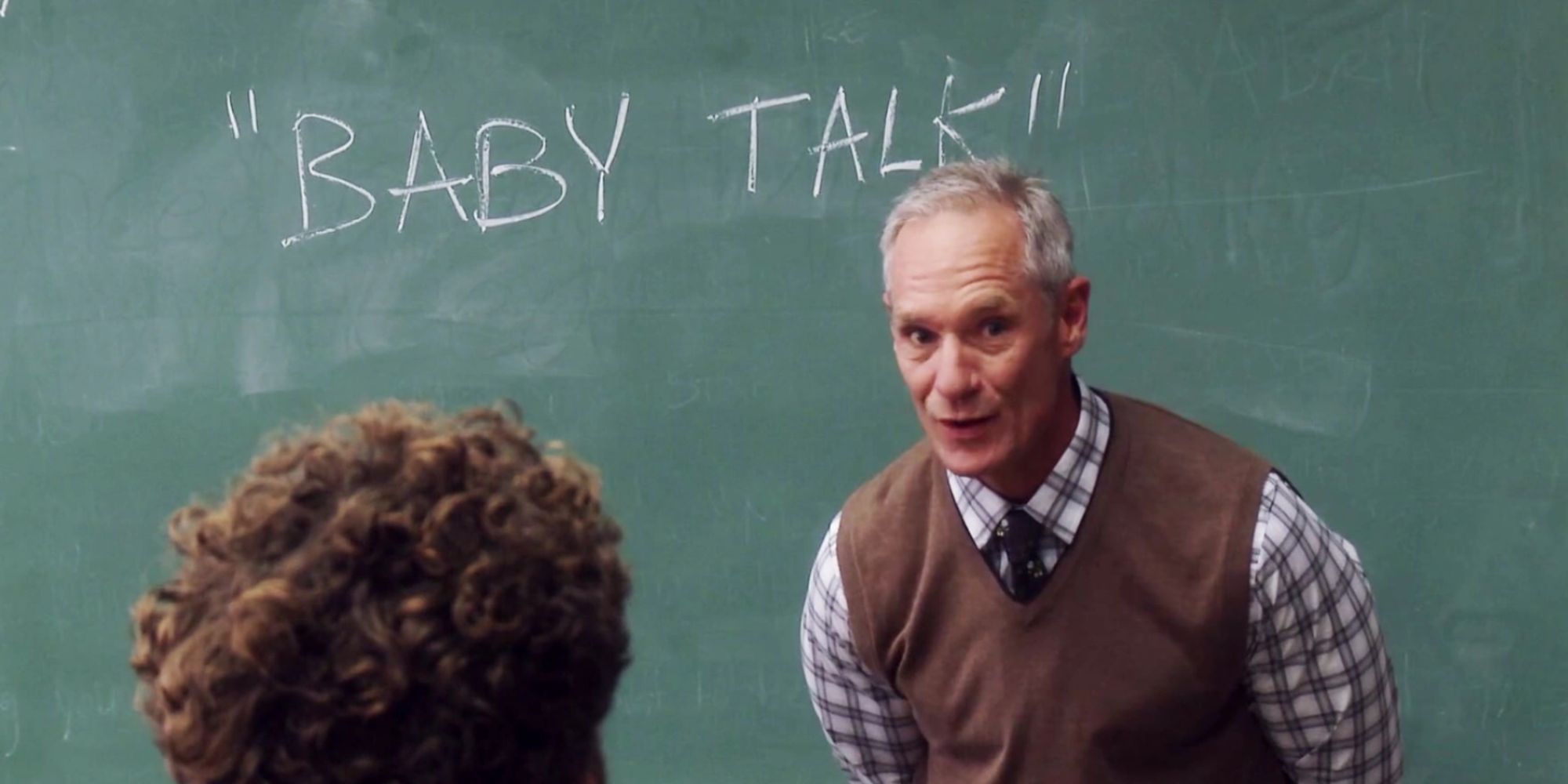 Still from 'Community': Professor in front of chalkboard that says 