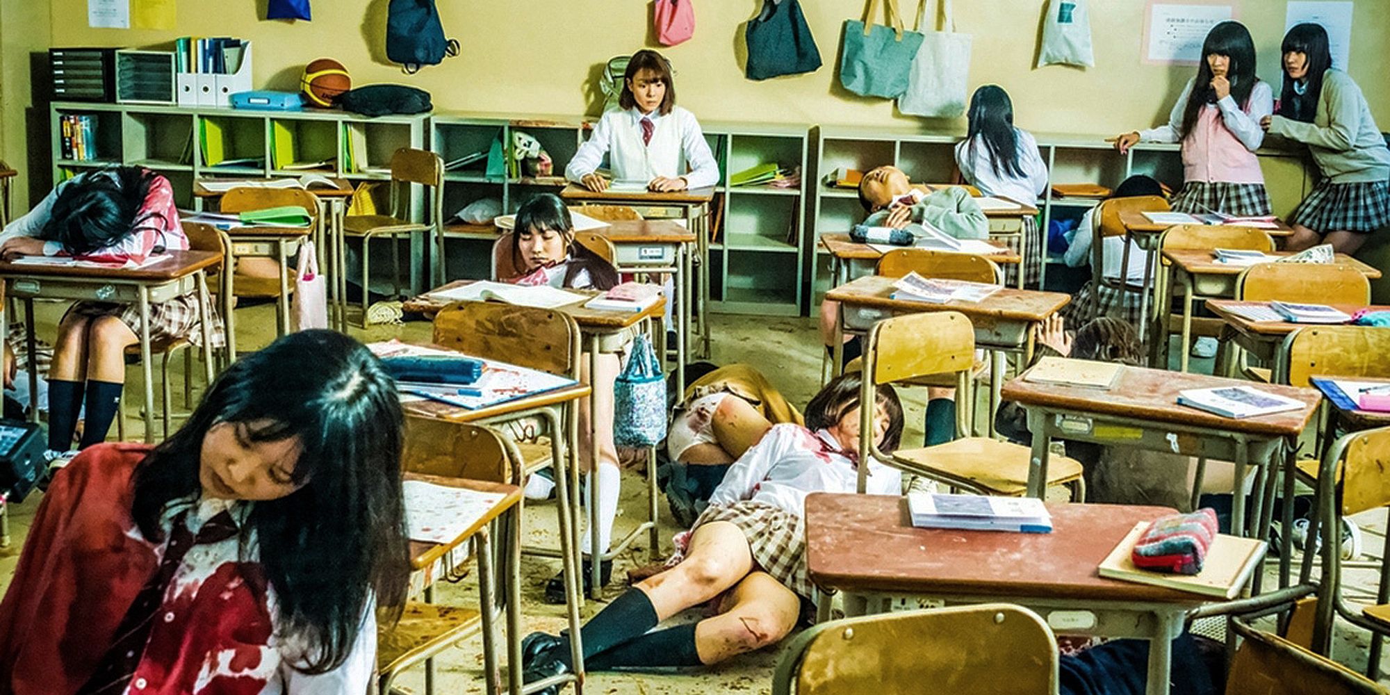 A girl sitting at the back of her class looks on in shock as her classmates lay around her dead and bloodied.