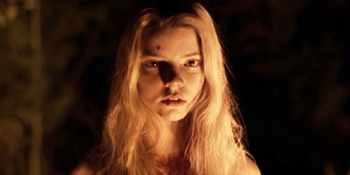 Thomasin (Anya Taylor-Joy) stands in the dark, illuminated by the glow of a fire. 