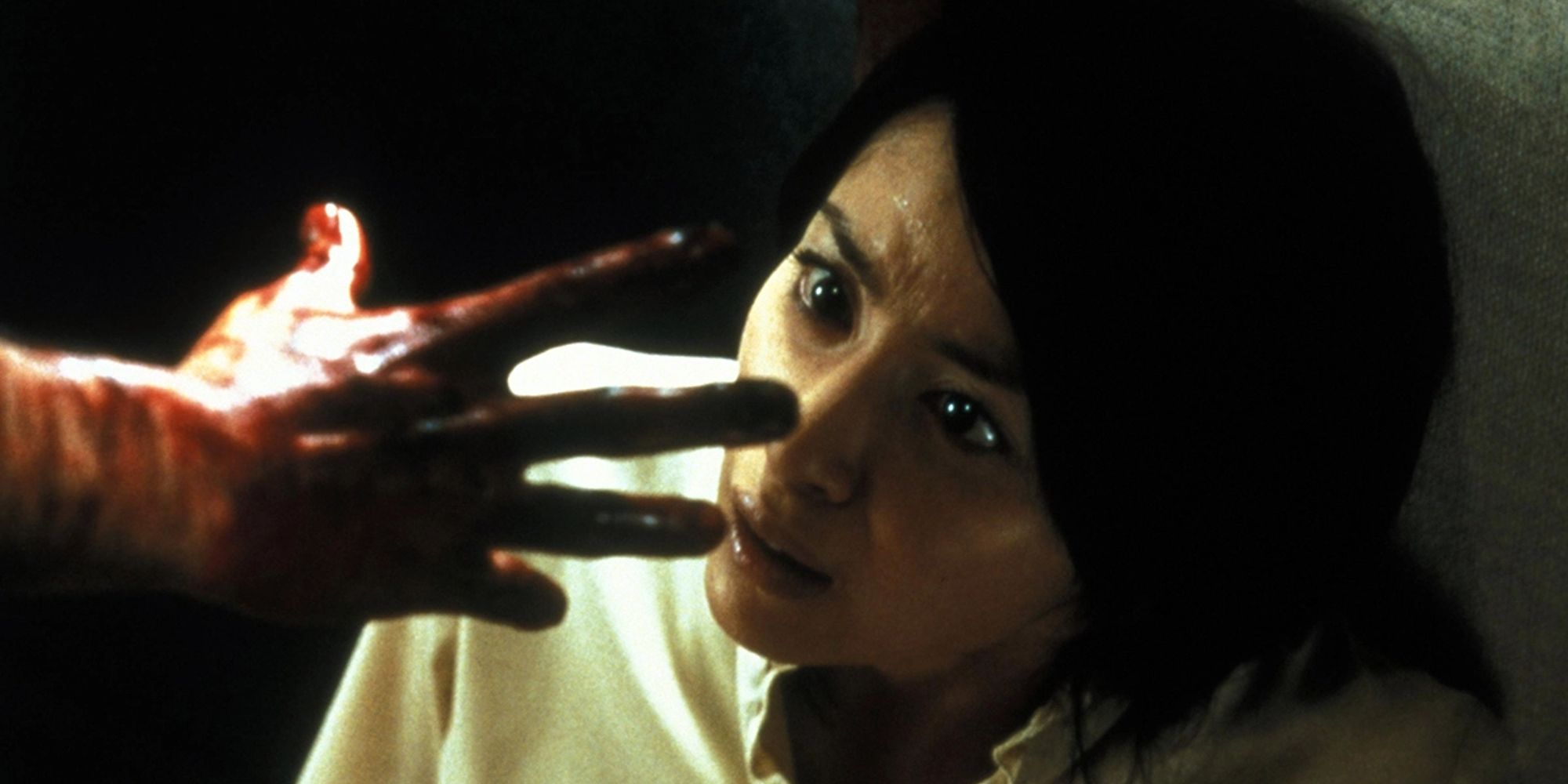 A terrified woman recoils as a bloodied hand reaches towards her face.
