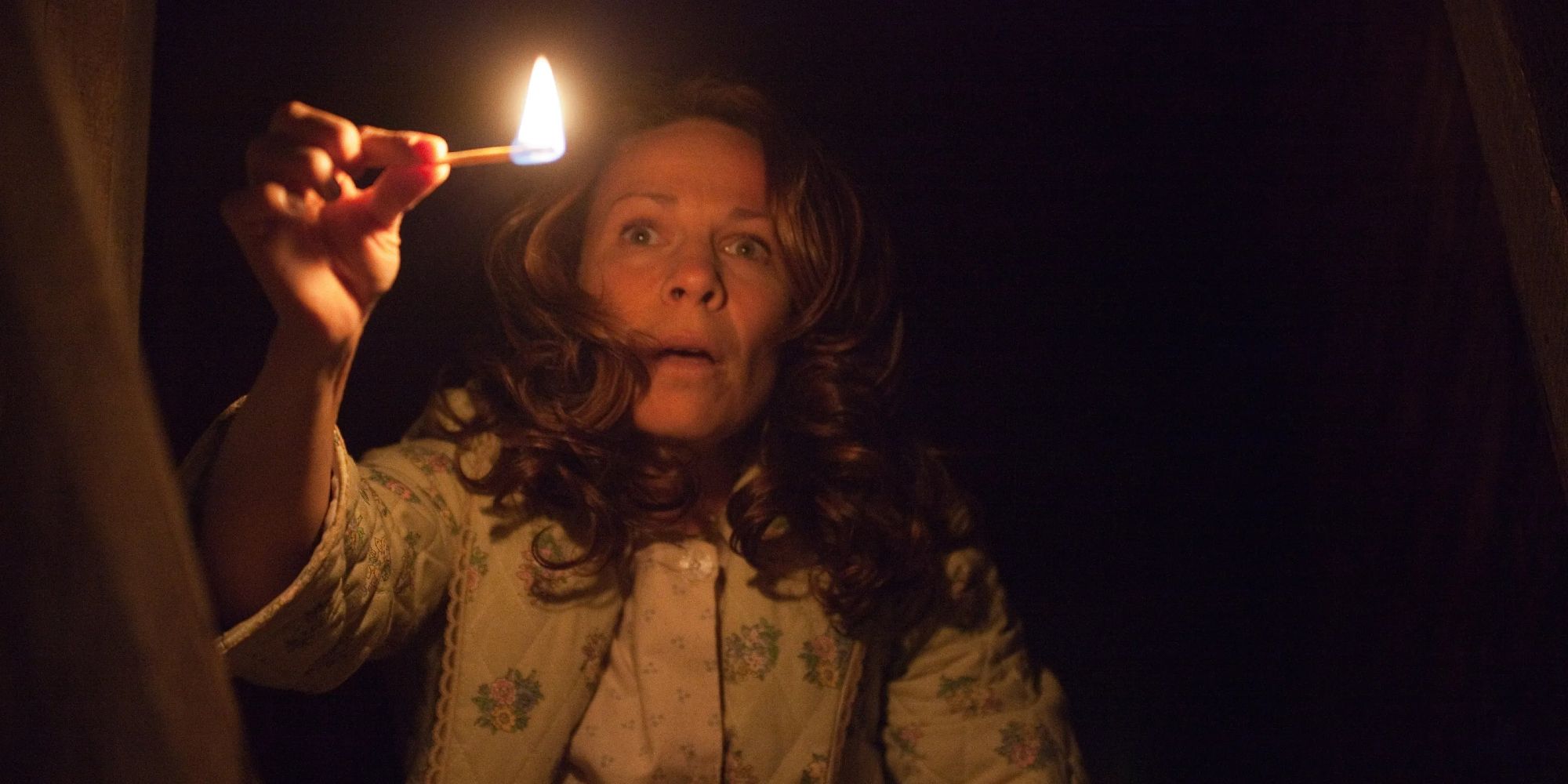 Lili Taylor as Carolyn Perron holding a lit match in the dark in The Conjuring