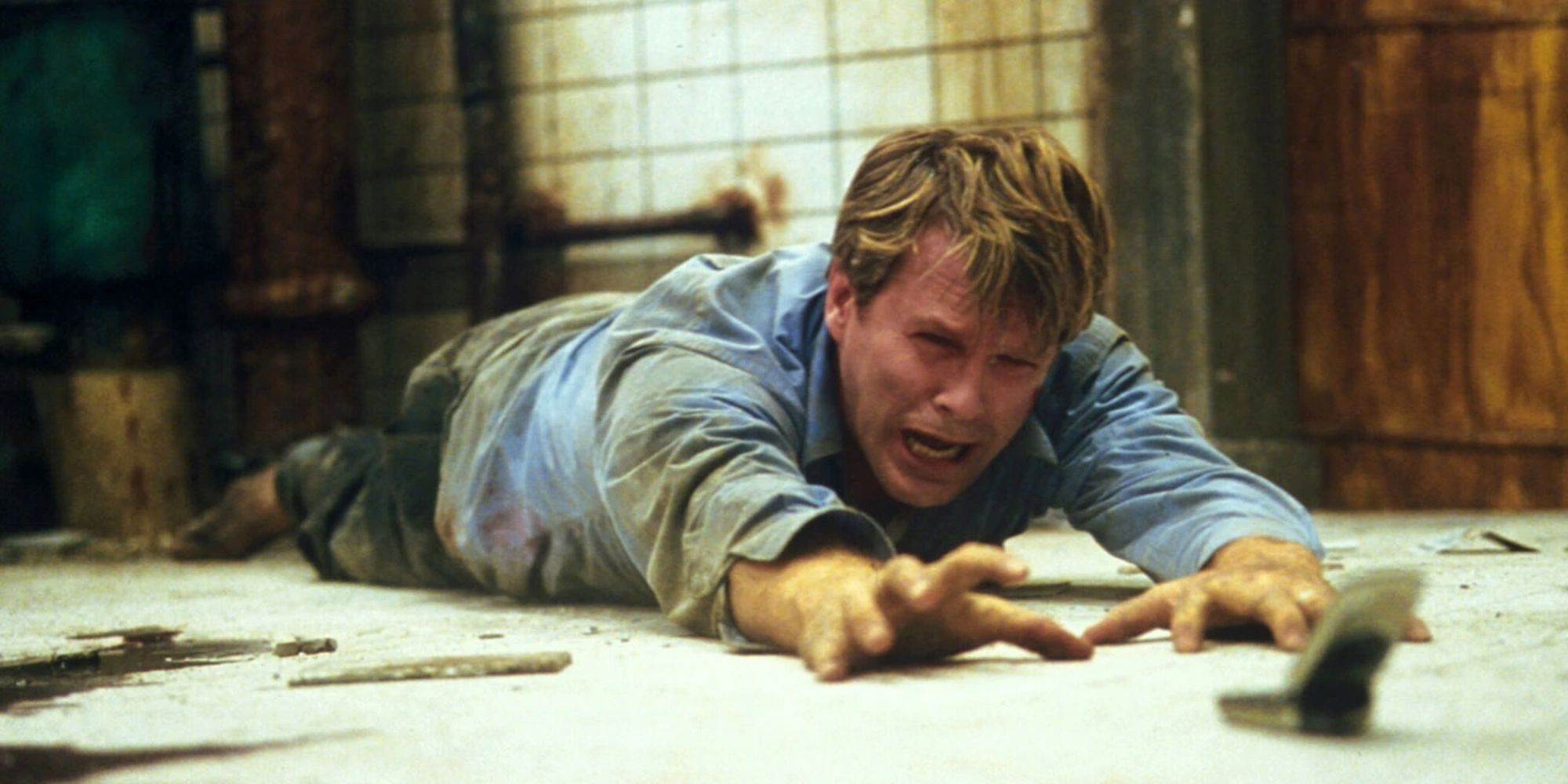 Cary Elwes tirado en el suelo y alcanzando el teléfono en la película Saw (2004)