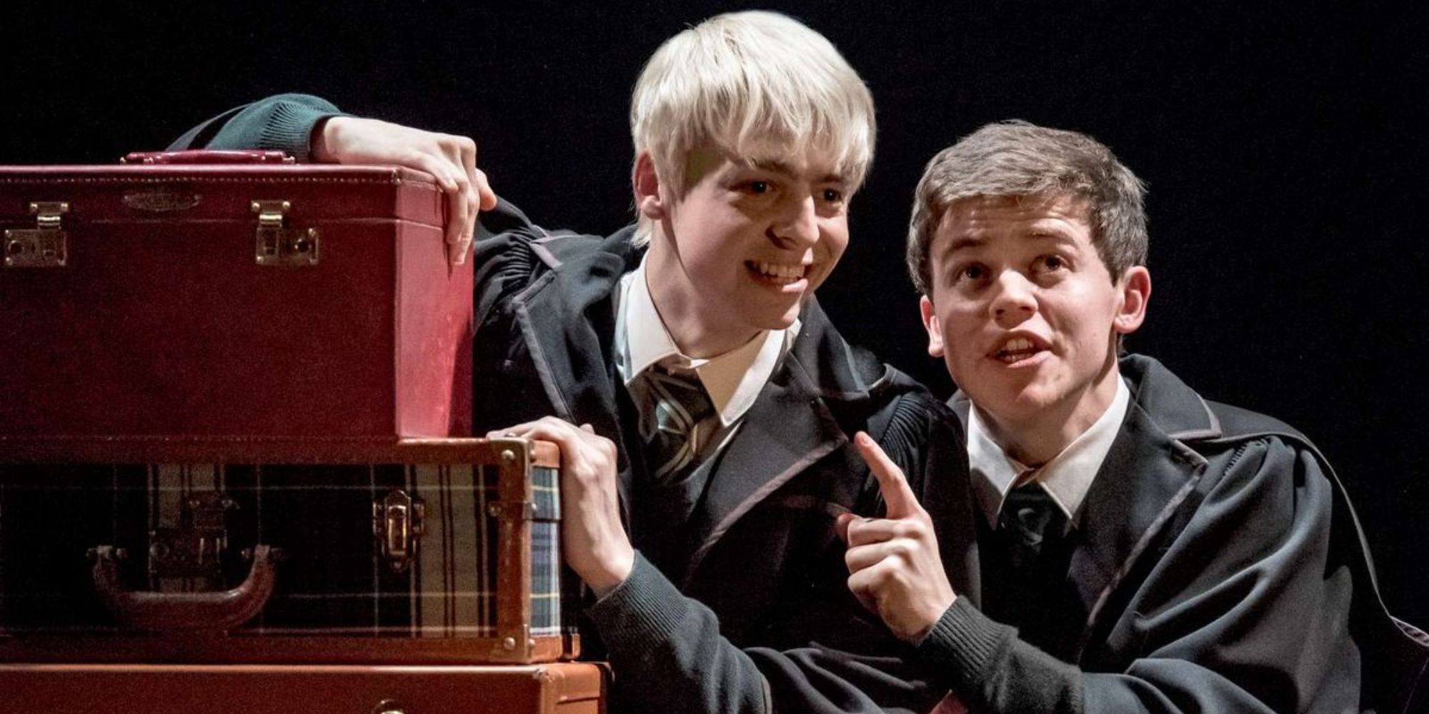 Albus Potter (Sam Clemmett) and Scorpius Malfoy (Anthony Boyle) crouch by some luggage in The Cursed Child.
