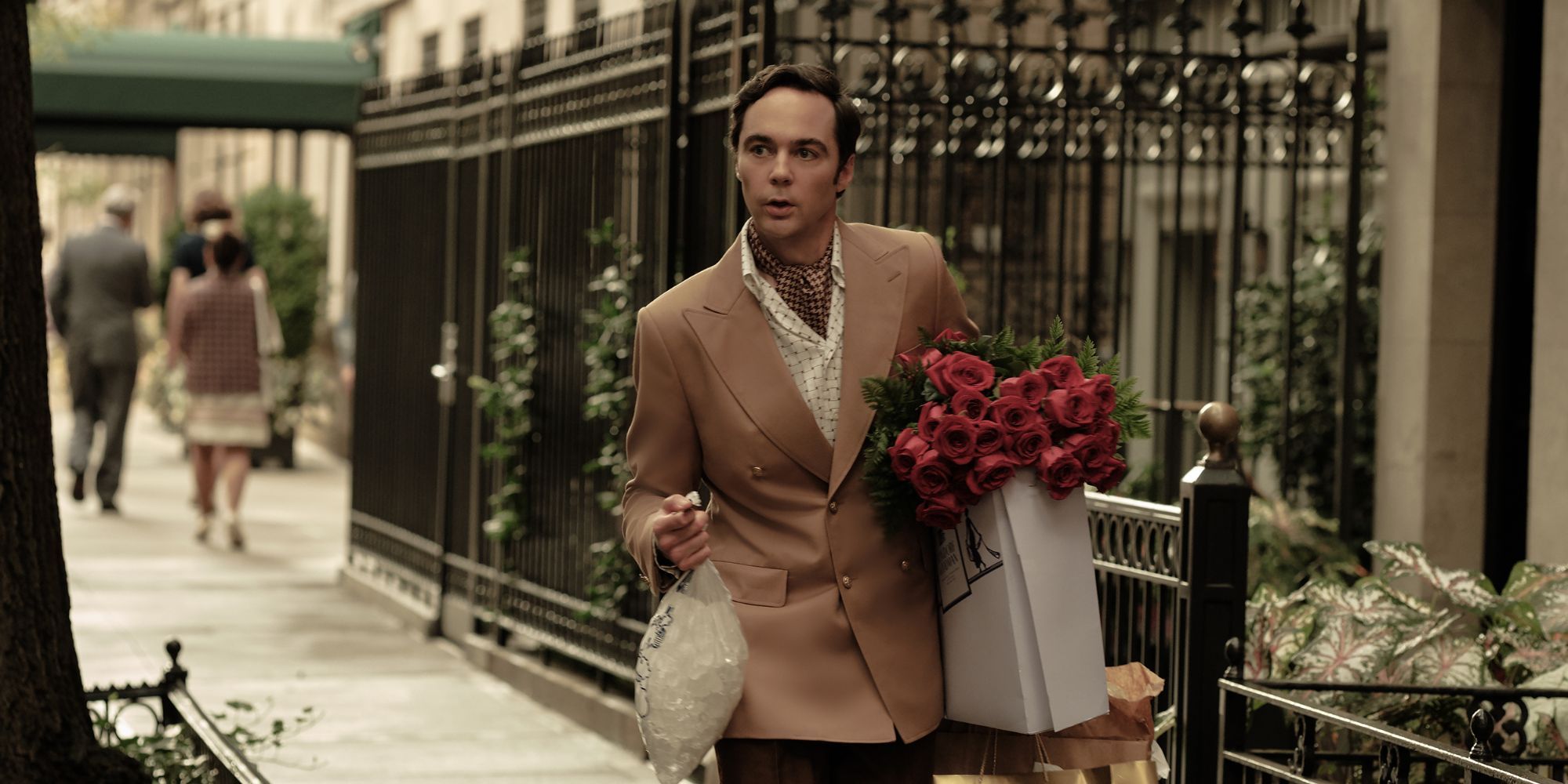 A man in suit carrying a bouquet of roses and a bag of ice, walking down the street