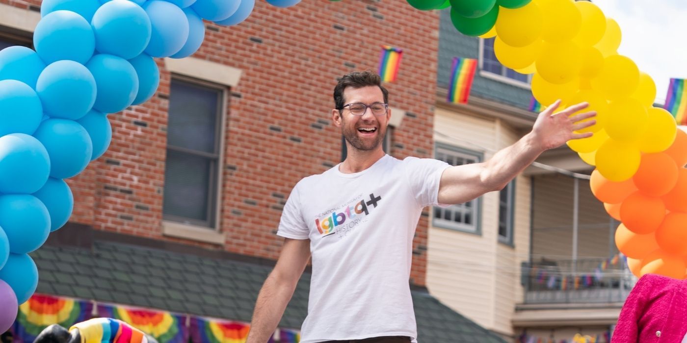 Bobby on a pride parade waving at the crowd and smiling in the 2022 film Bros