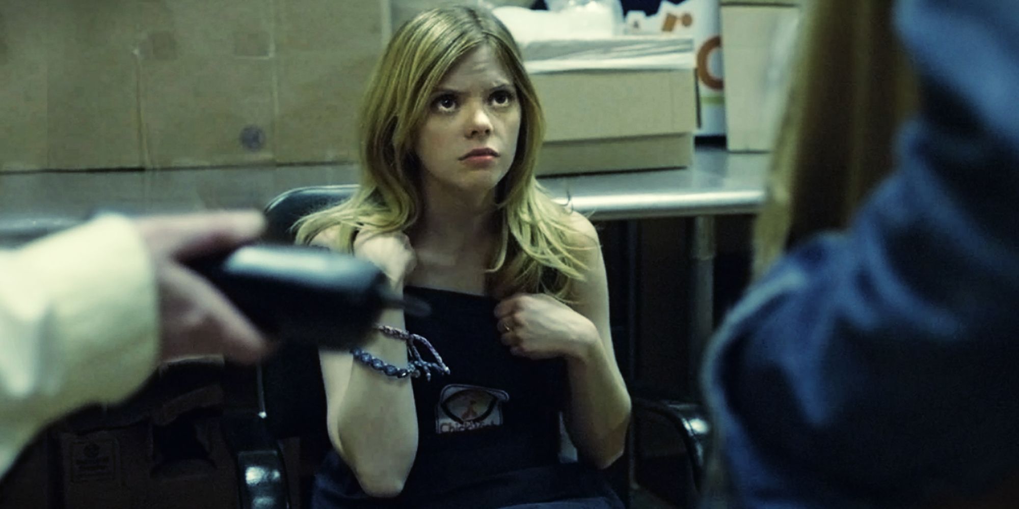 Dreama Walker as Becky sitting in a chair in front of two people in Compliance