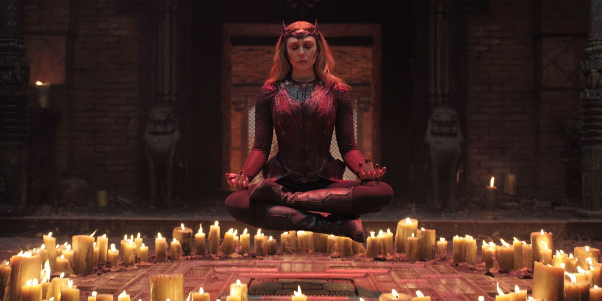 Uma mulher toda de vermelho está meditando acima do solo com muitas velas ao seu redor