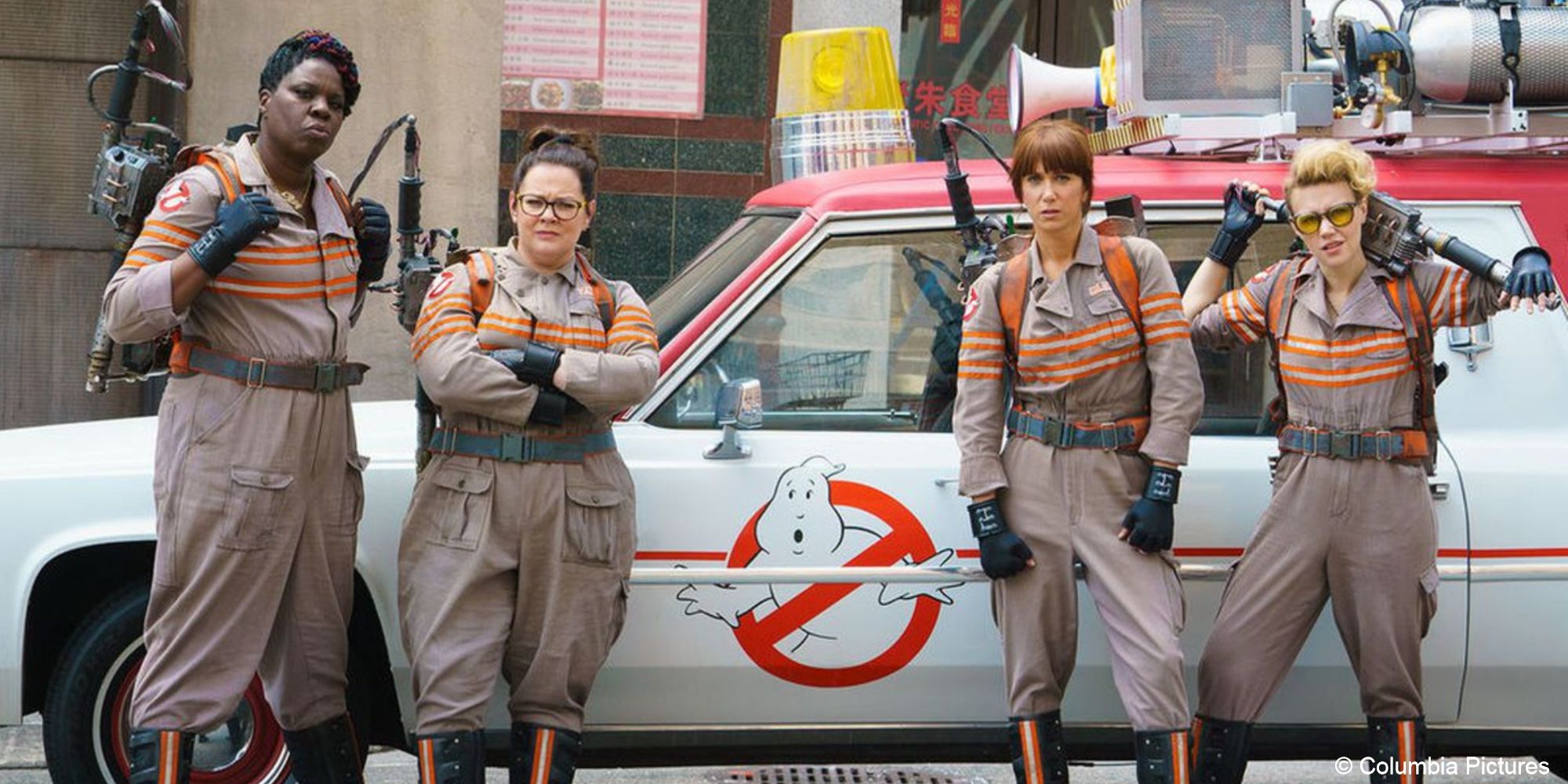 Los Cazafantasmas Patty Abby parada frente a Ecto-1 con equipo de Los Cazafantasmas Erin y Jillian