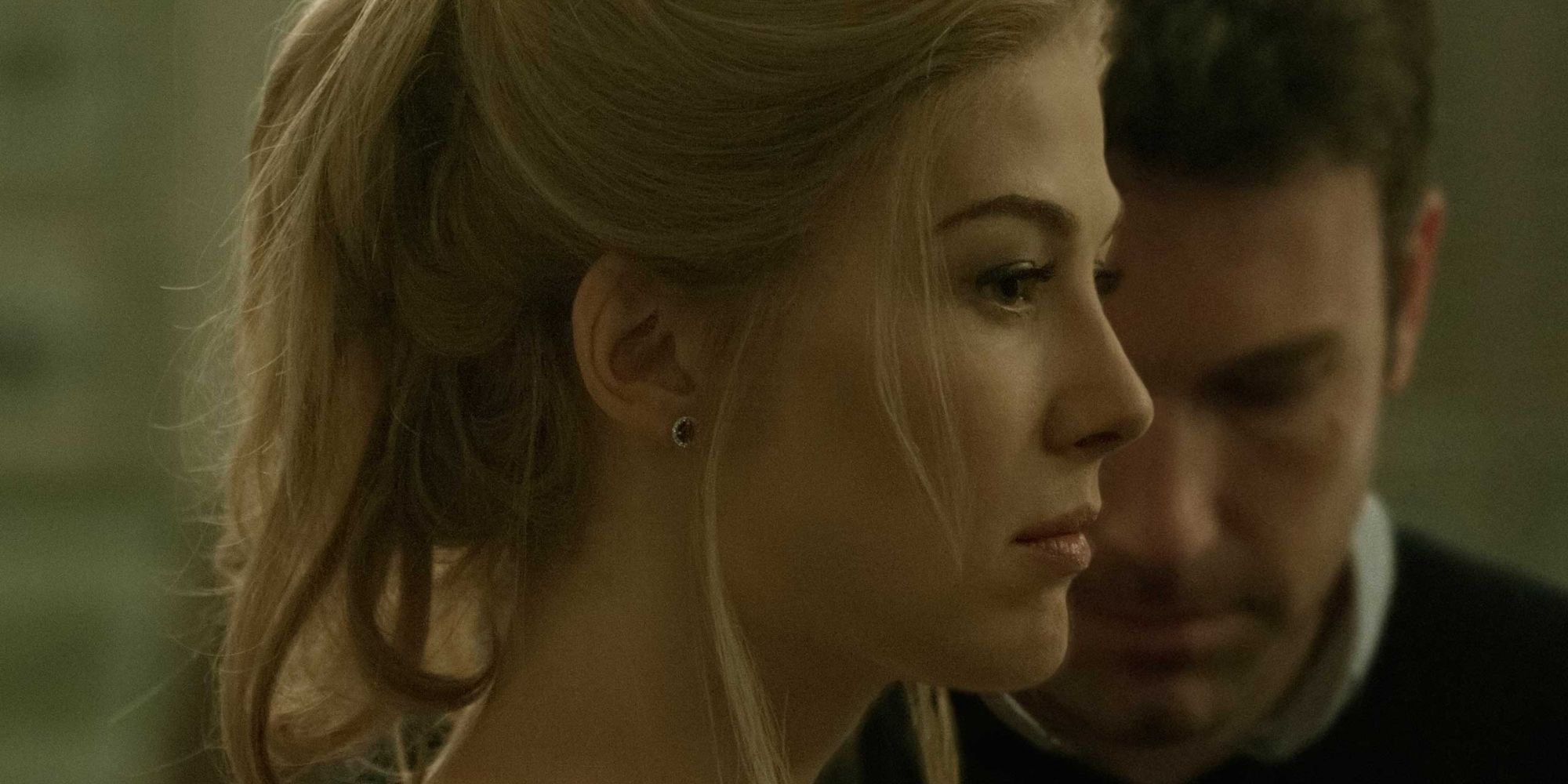 A profile close up shot of Rosamund Pike with Ben Affleck in the background in Gone Girl