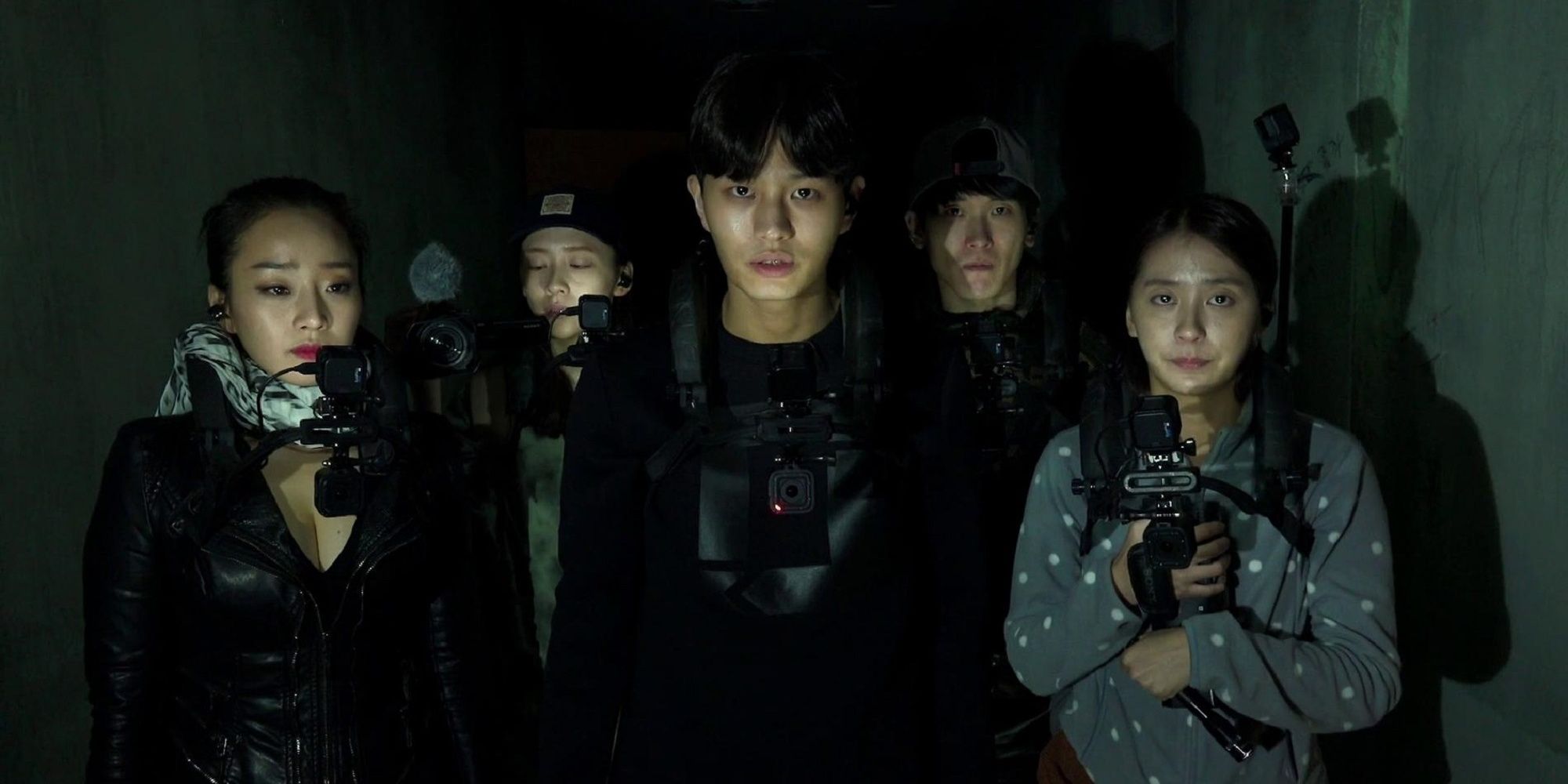 Five young people with body cameras walk through a dark building and look ahead in Gonjiam Haunted Asylum.
