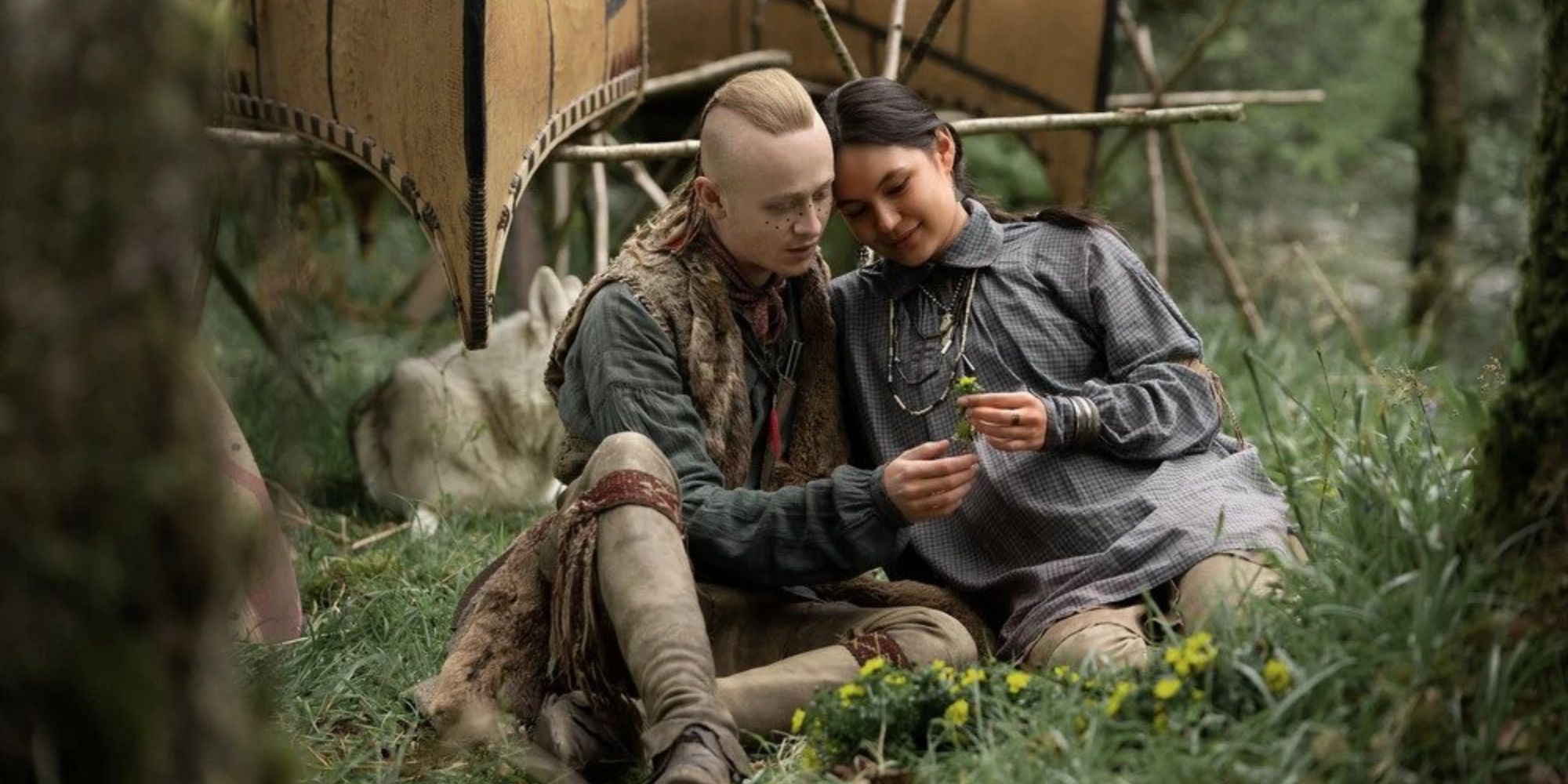 Emily (Wahionhaweh) and Ian sitting in a meadow looking at a flower Emily is holding.