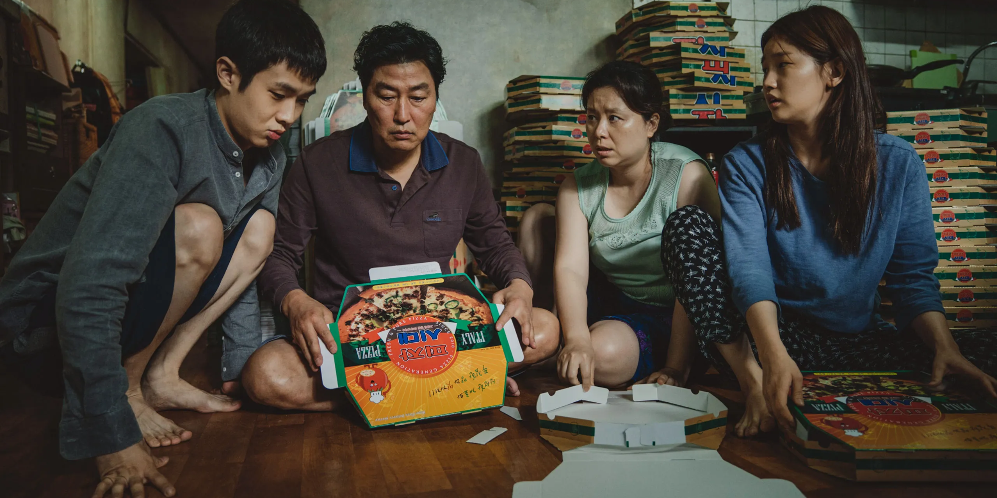 The cast of Parasite sits on the floor with folded pizza boxes to earn money.