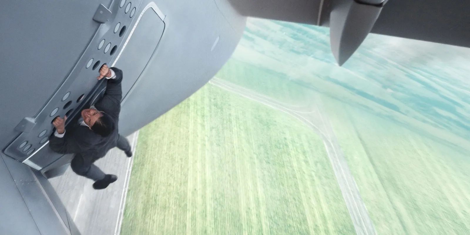 Ethan Hunt (Tom Cruise) hangs on to the door of an airplane as it takes off.