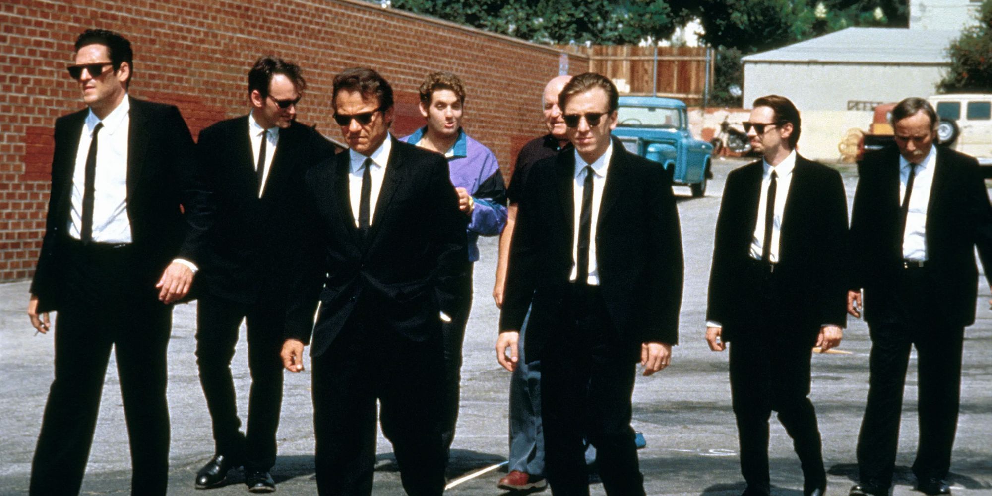 The cast of Reservoir Dogs walking together and wearing black suits 