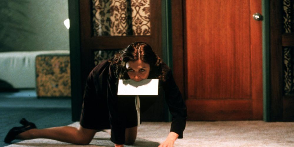 Maggie Gyllenhaal como Lee rastejando no chão enquanto segura um envelope entre os dentes em Secretária