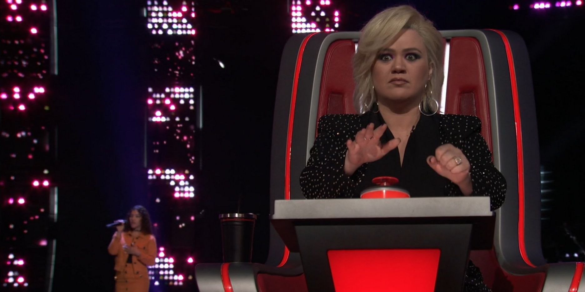 Kelly Clarkson assise sur une chaise tandis qu'une femme chante derrière elle dans l'émission 