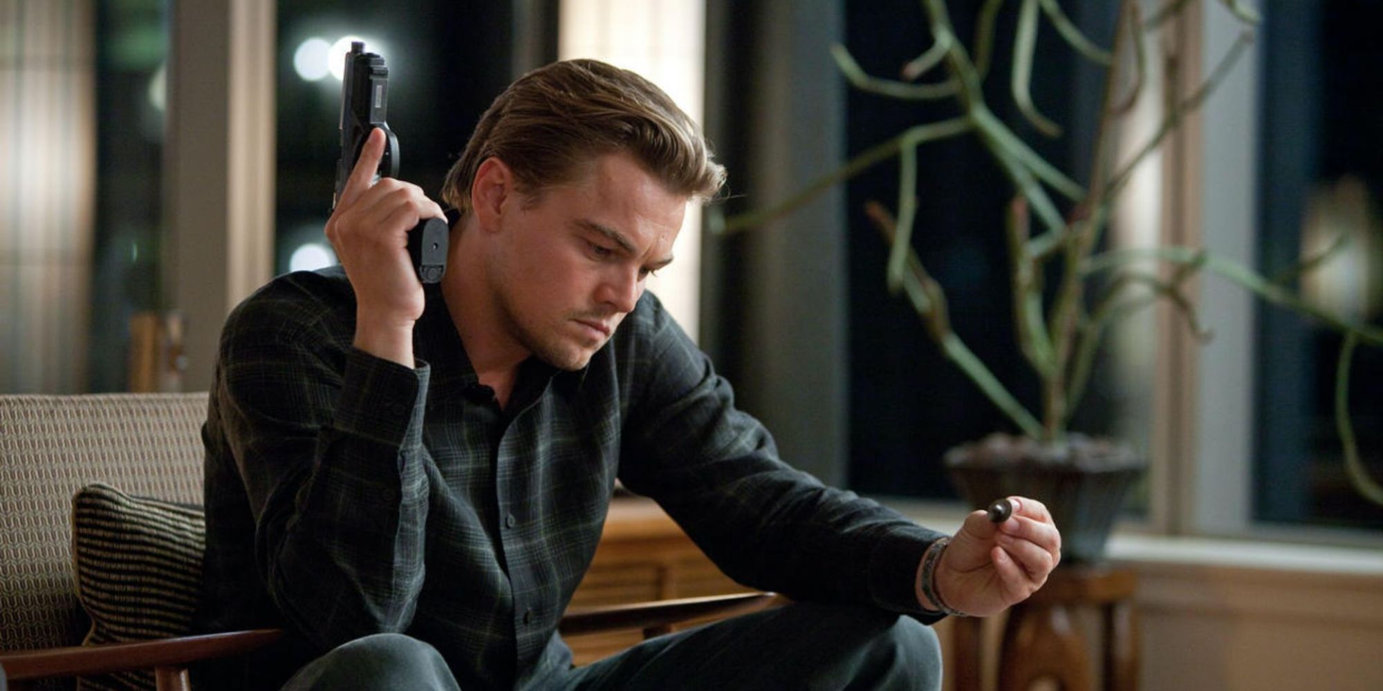 Leonardo DiCaprio como Cobb, sentado y mirando su tótem mientras sostiene un arma al comienzo de la película.
