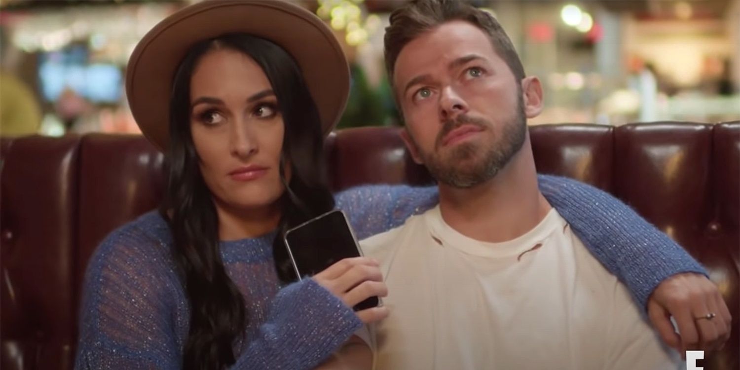 Artem Chigvintsev and Nikki Bella look in different directions in a restaurant on Total Bellas