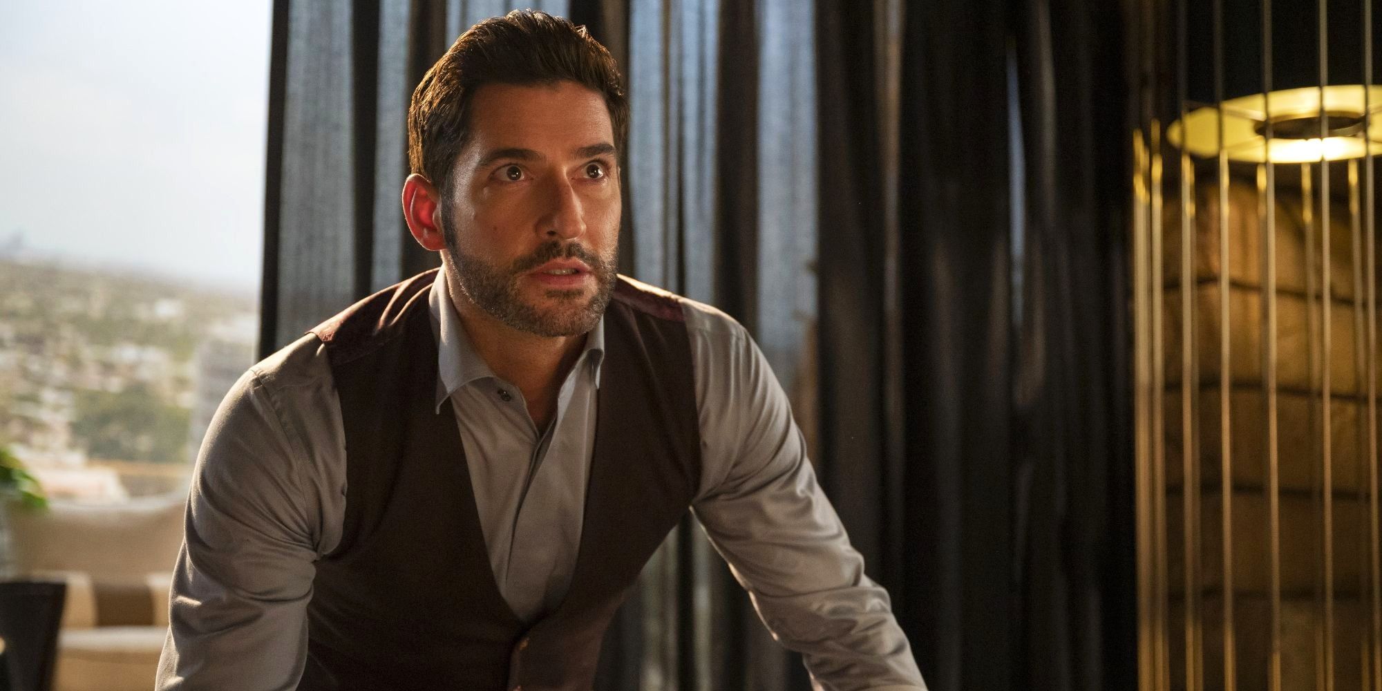 Tom Ellis as Lucifer Morningstar in Lucifer leaning over a desk, looking surprised.