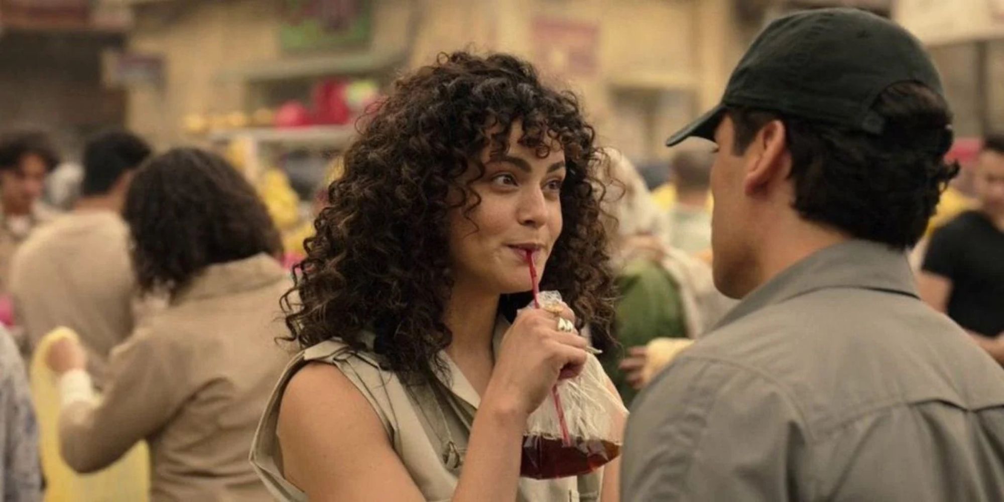 A curly-haired woman is drinking from a plastic bag while talking to a man