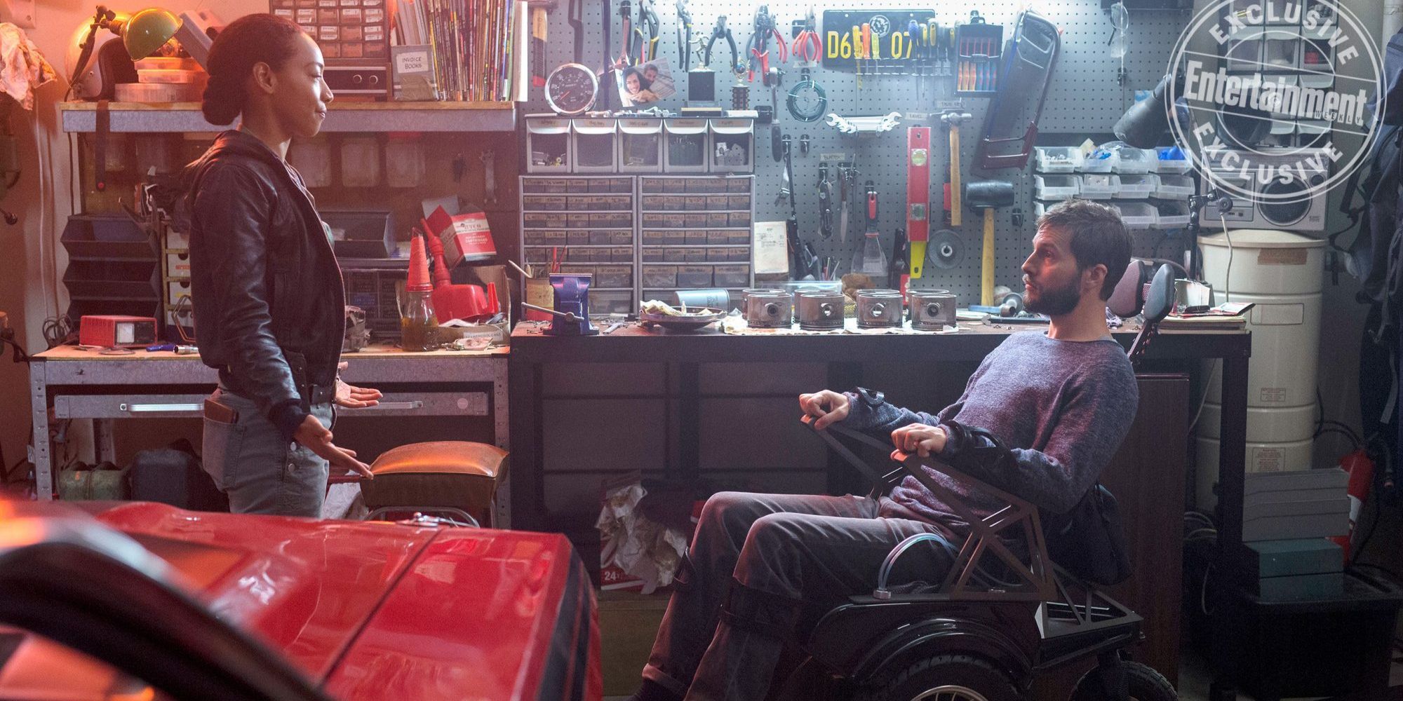 A man in the wheelchair is talking to a woman in a garage