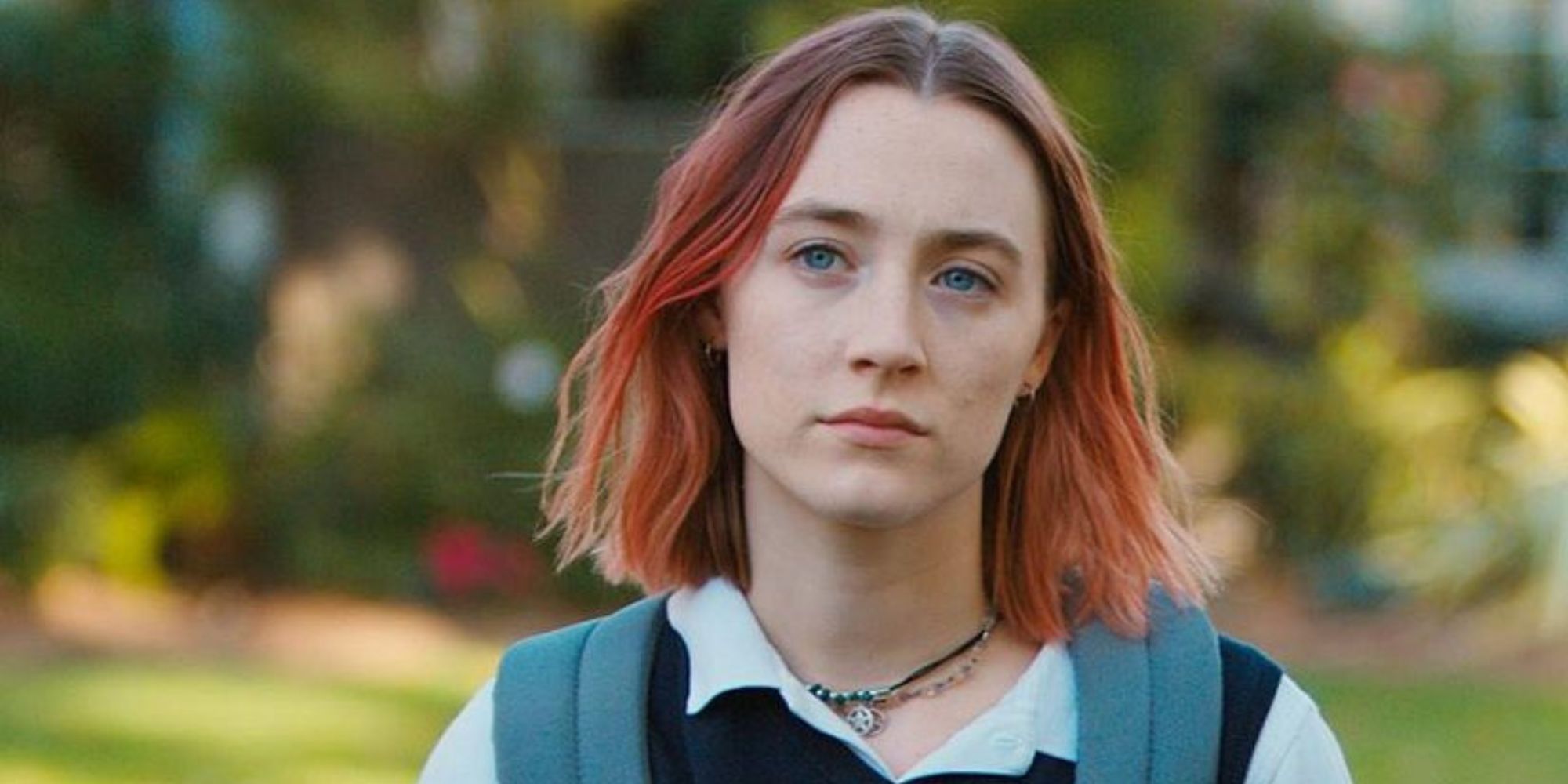 Lady Bird standing in an open space with trees in the background in Lady Bird.