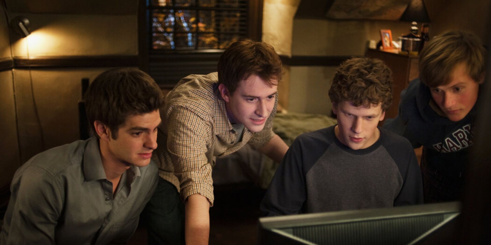 Four men staring at a computer screen in a dorm room