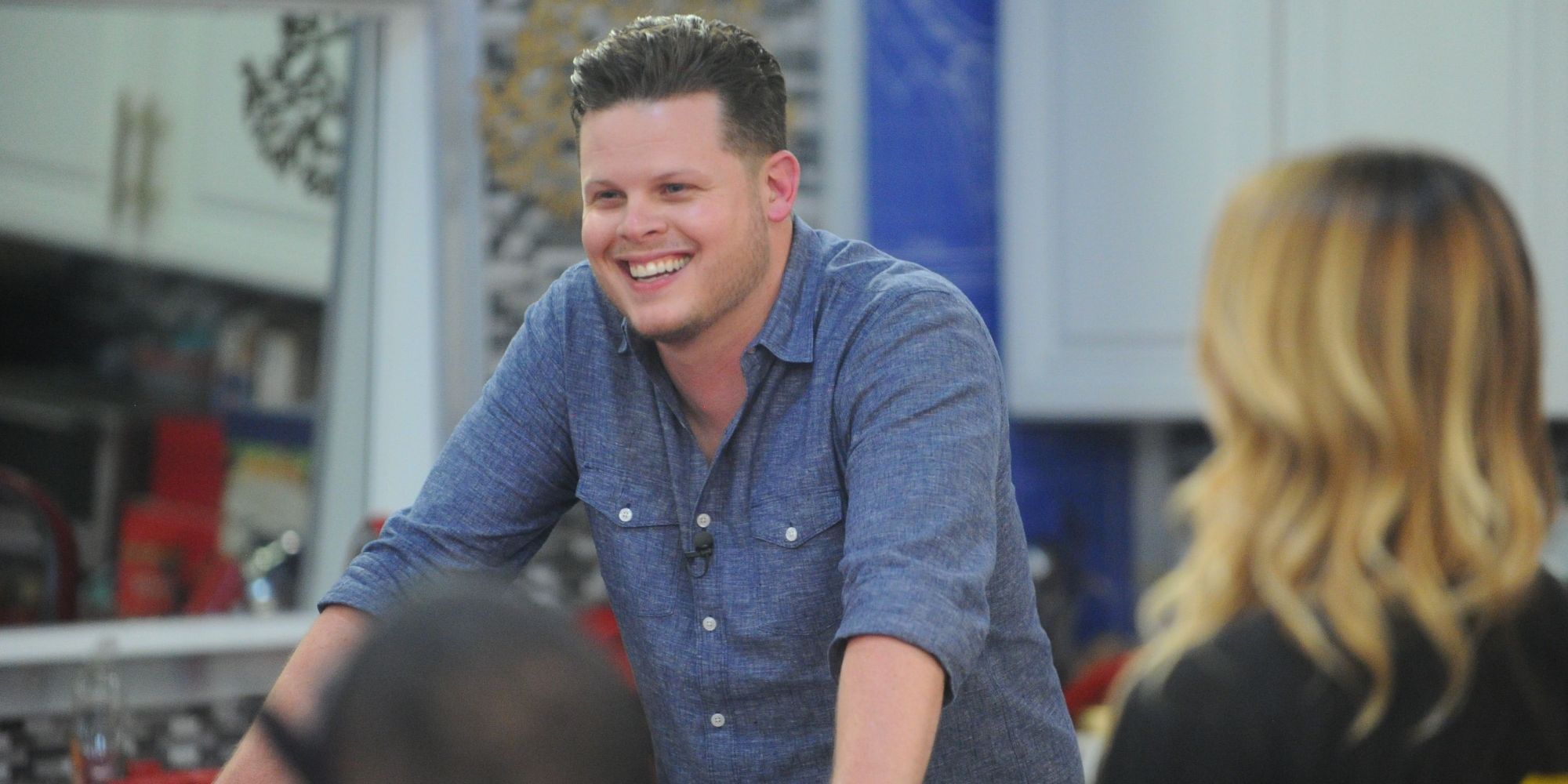 Derrick Levasseur on Big Brother leaning over a counter, smiling.