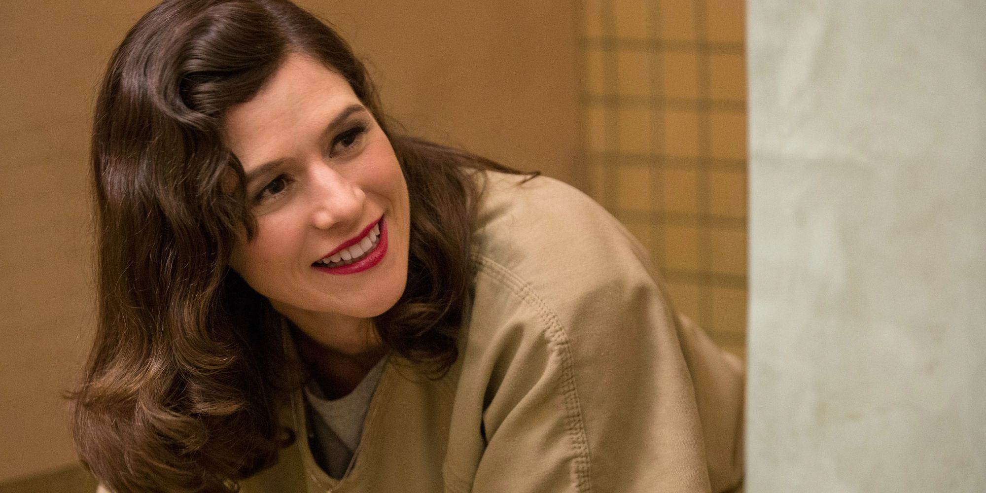 Yael Stone as Lorna Morello looking around a corner and smiling in Orange is the New Black