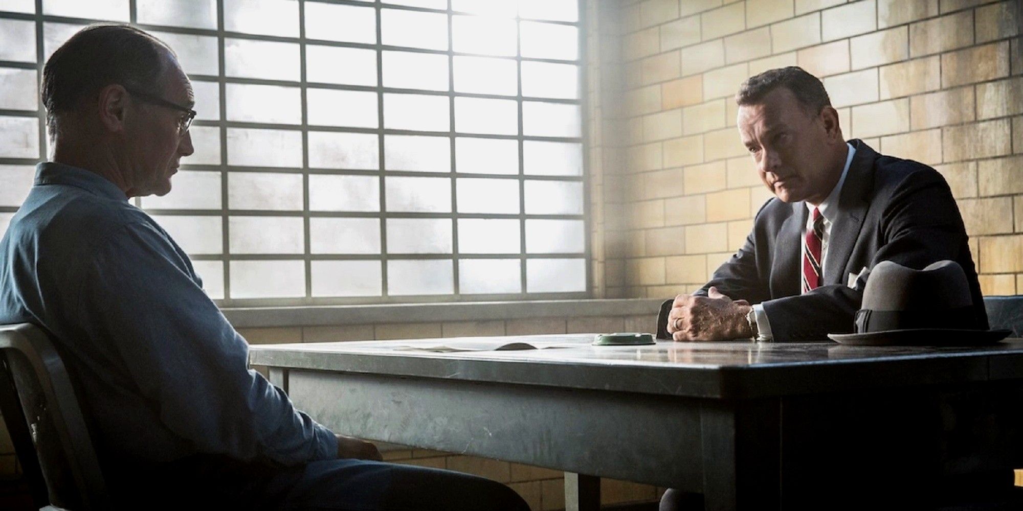 Dois homens sentados à mesa numa sala de interrogatório