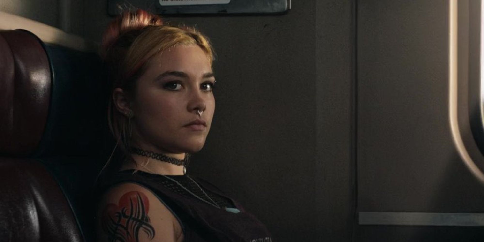 A young woman with face piercing and tattos looks annoyed on a train