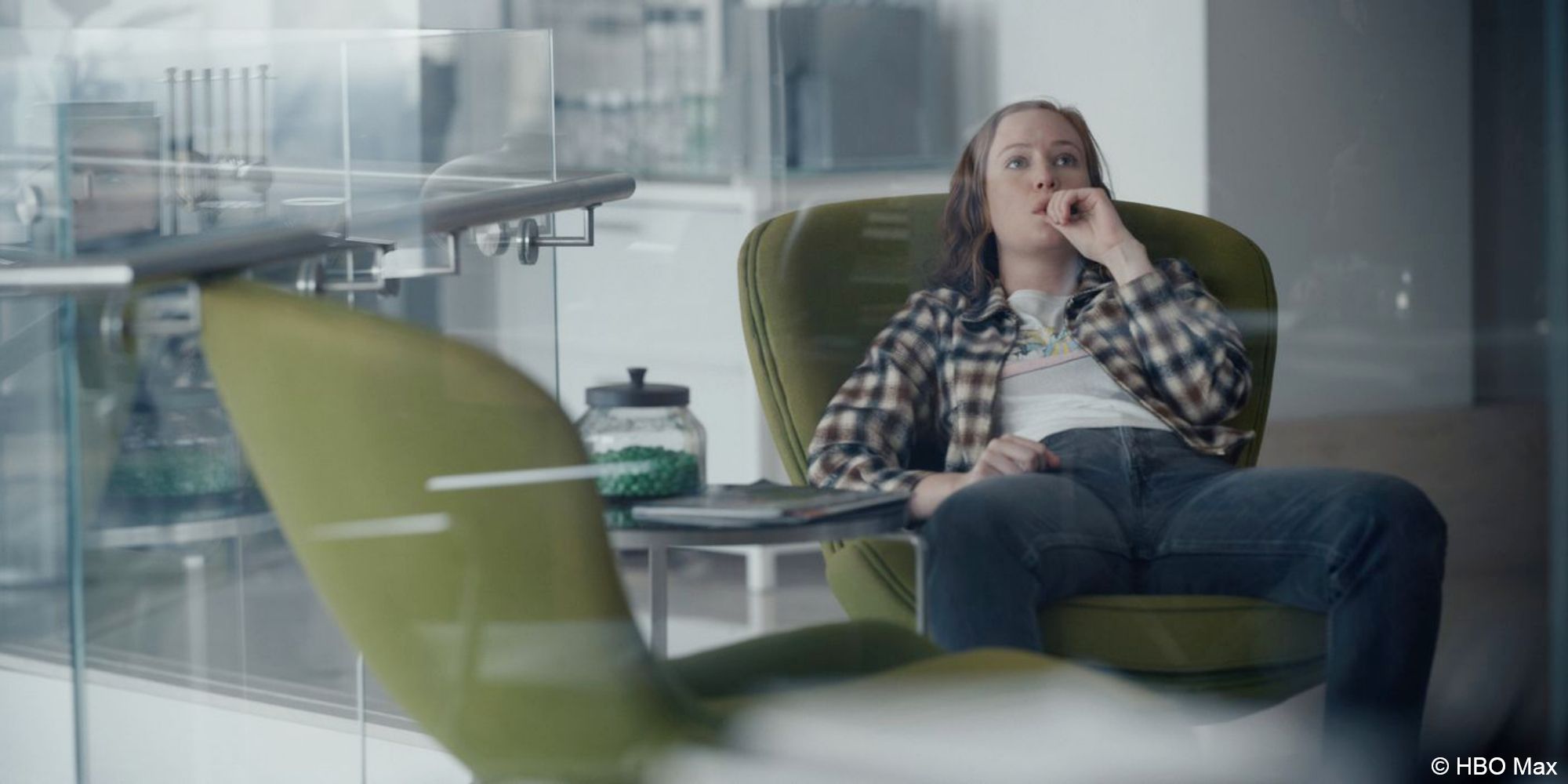 Hacks_Ava sits in an office slouched in a green chair chewing her thumbnail