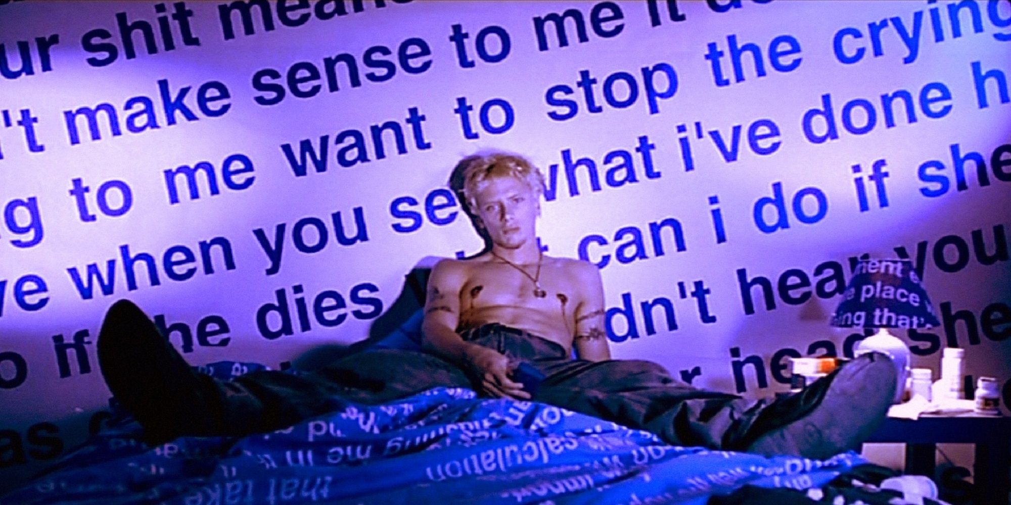 Montgomery sits on a bed with words projecting onto the wall in Nowhere.