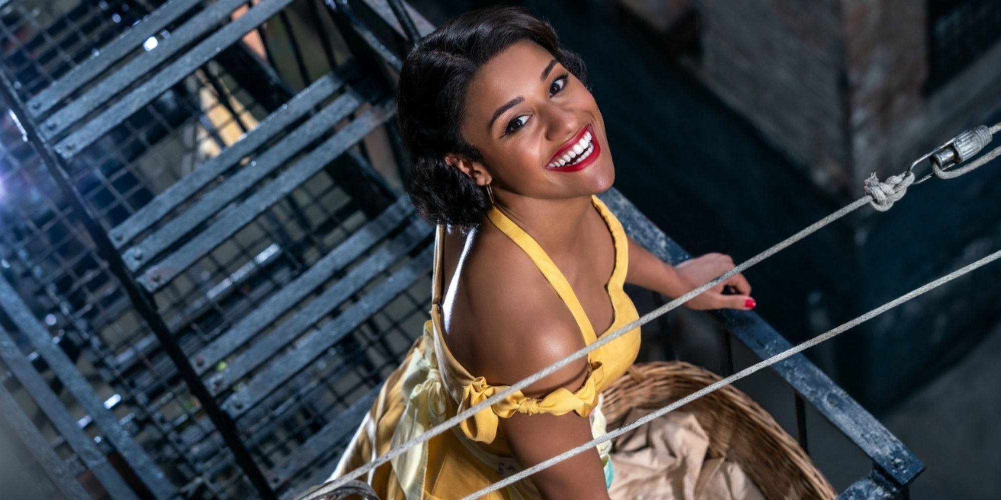 Anita (Ariana DeBose) sur un escalier de secours, souriant à la caméra dans West Side Story.