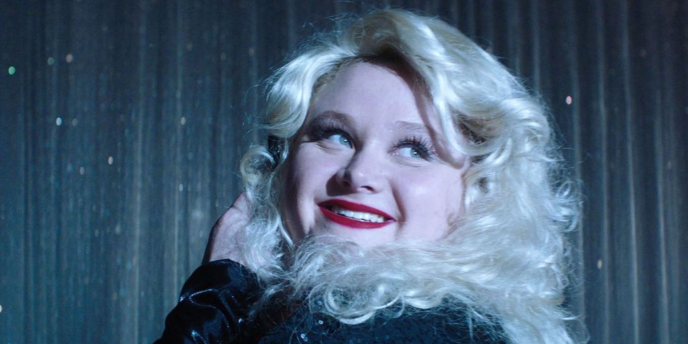 Dumplin', played by Danielle Macdonald, in red lipstick and blonde curls smiling over her shoulder at the camera. 