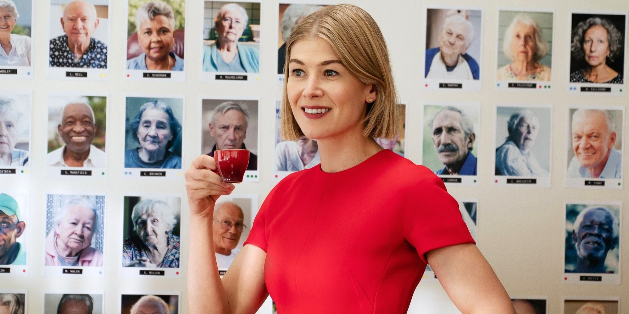 Rosamund Pike, que interpreta a Marla Grayson, sonríe frente a una pizarra cubierta de fotografías de I Care a Lot (2020)