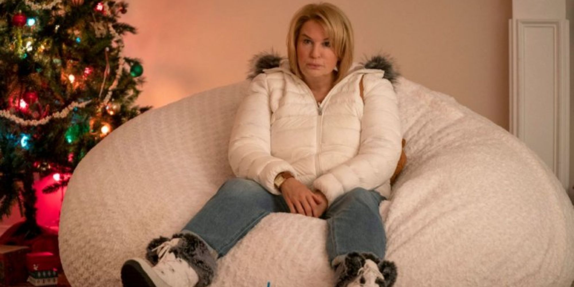 a blonde woman sitting on a bean bag chair next to a christmas tree