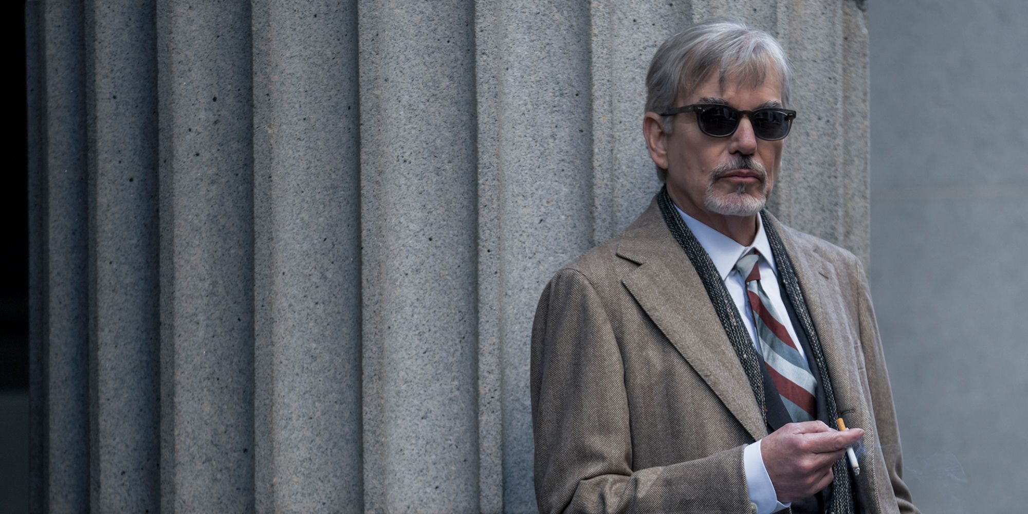 a man in suit and sunglasses smoking next to a concrete poll