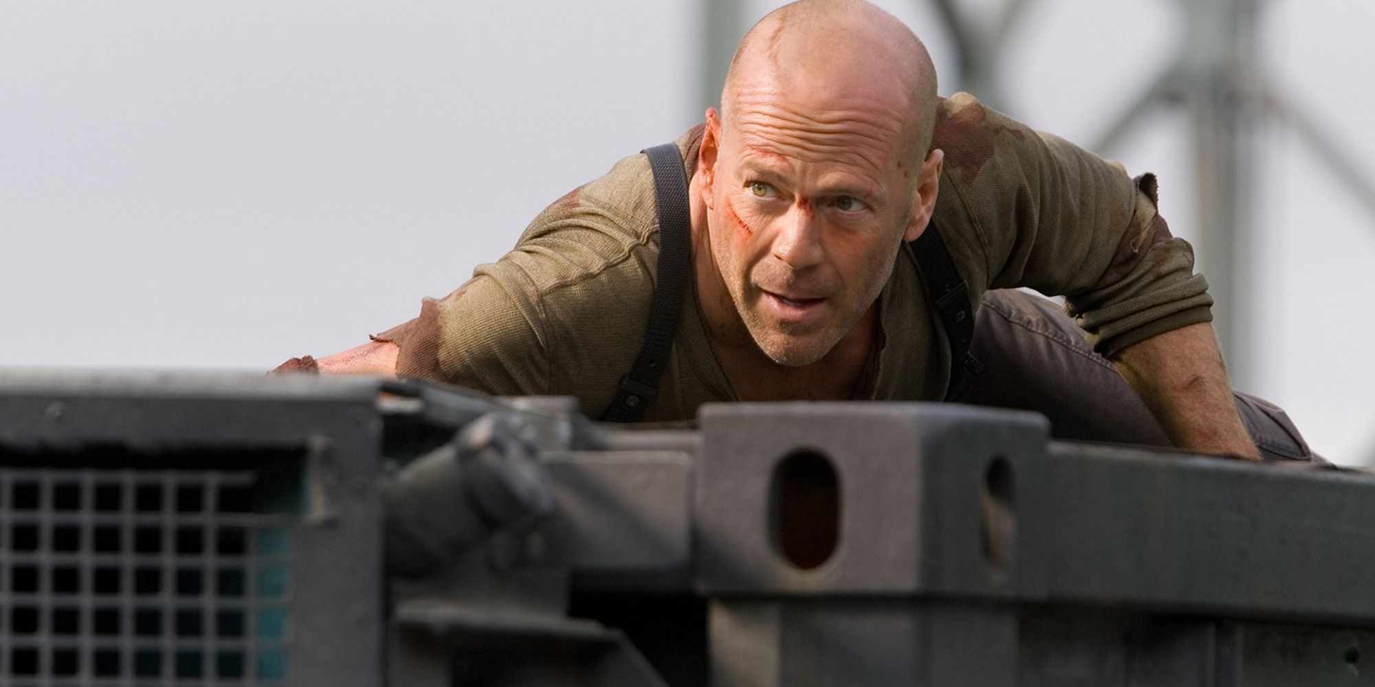Bruce Willis hides from someone on top of a metal structure in Die Hard