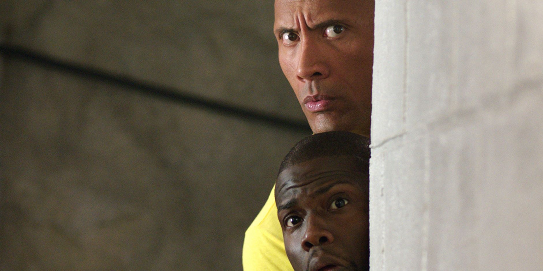 Dwayne Johnson and Kevin Hart looking from behind a wall in 'Central Intelligence'