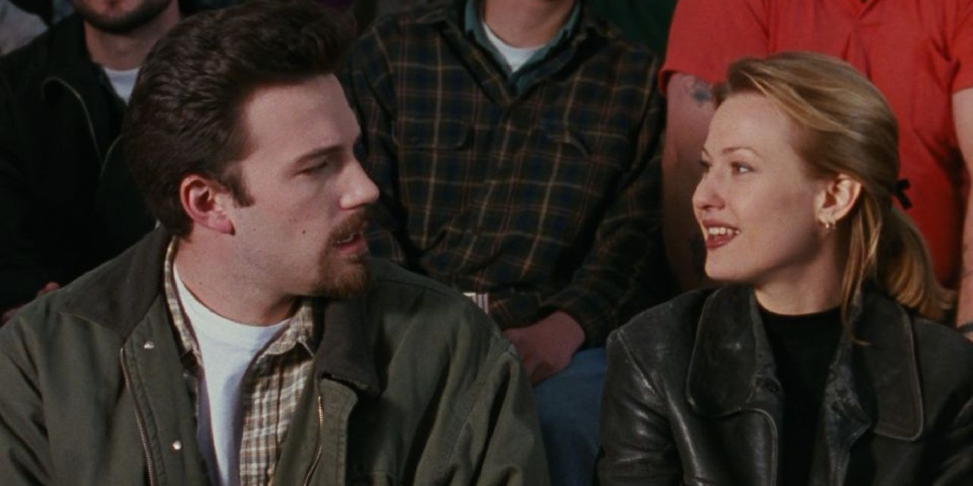 A man and a woman look at one another while sitting in a crowd in a scene from Chasing Amy.