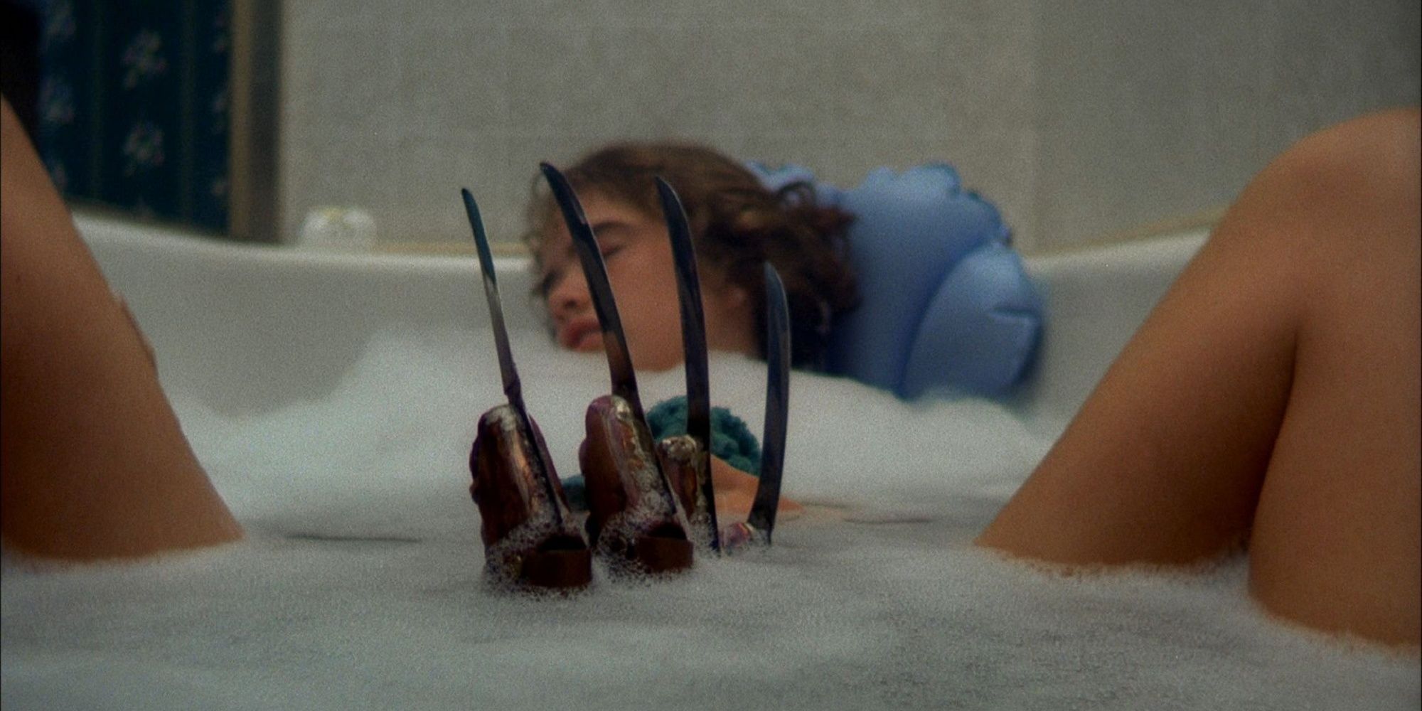 Heather Langenkamp sleeps in the bath as a claw rises beneath her legs in A Nightmare on Elm Street