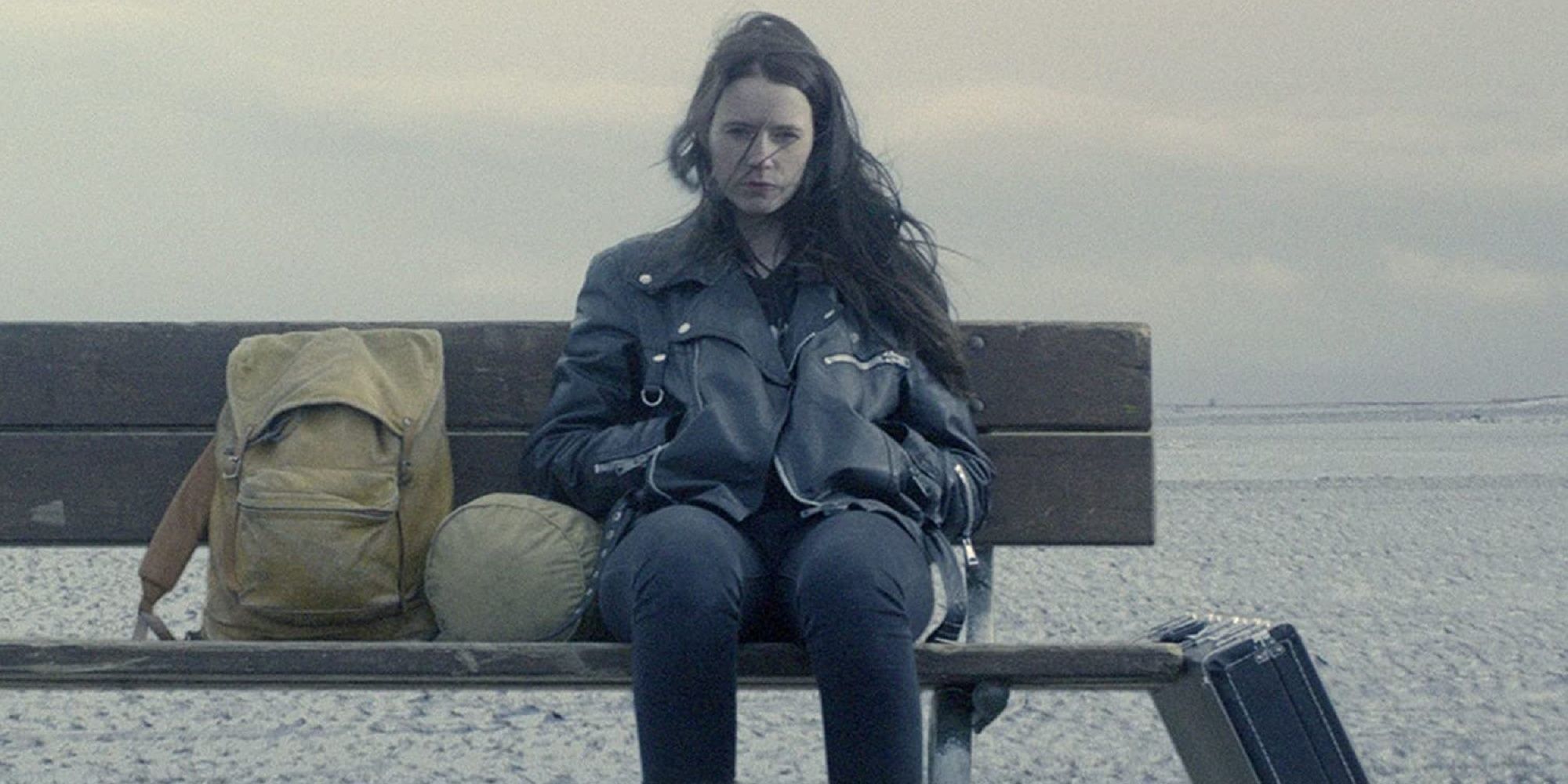 Hera sitting on a bench in the middle of nowhere with her leather jacket in Metalhead.